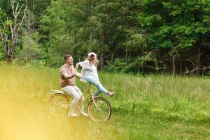 Two people riding bicycles together through a lush green meadow on a sunny summer day.
