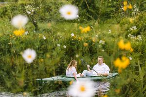 A couple enjoys a romantic boat ride through a tranquil pond surrounded by blooming yellow wildflowers and lush greenery.