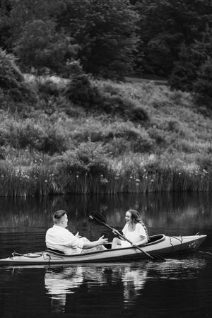 A black and white photograph of two people paddling in a kayak on a serene lake surrounded by nature.