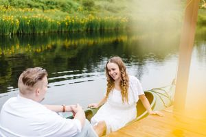 A couple sits together on a dock by a serene lake during golden hour, creating a romantic summer atmosphere.