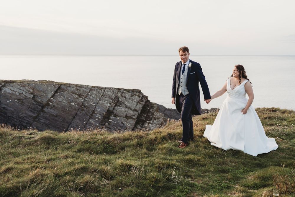 Bride and groom walking along coastal path during golden hour at the Cliff hotel