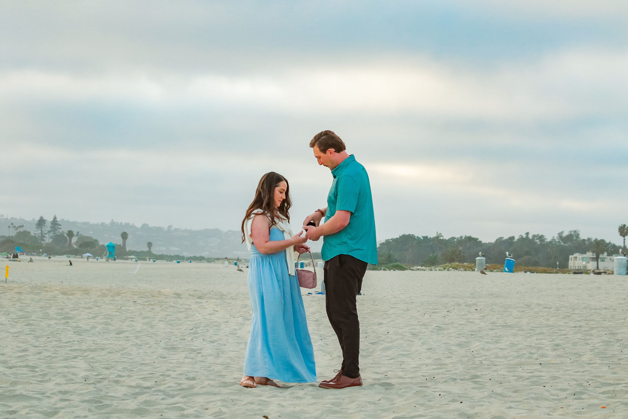 Newly engaged couple admiring the ring together on the beach by Zeus Holbrook San Diego Wedding Photographer