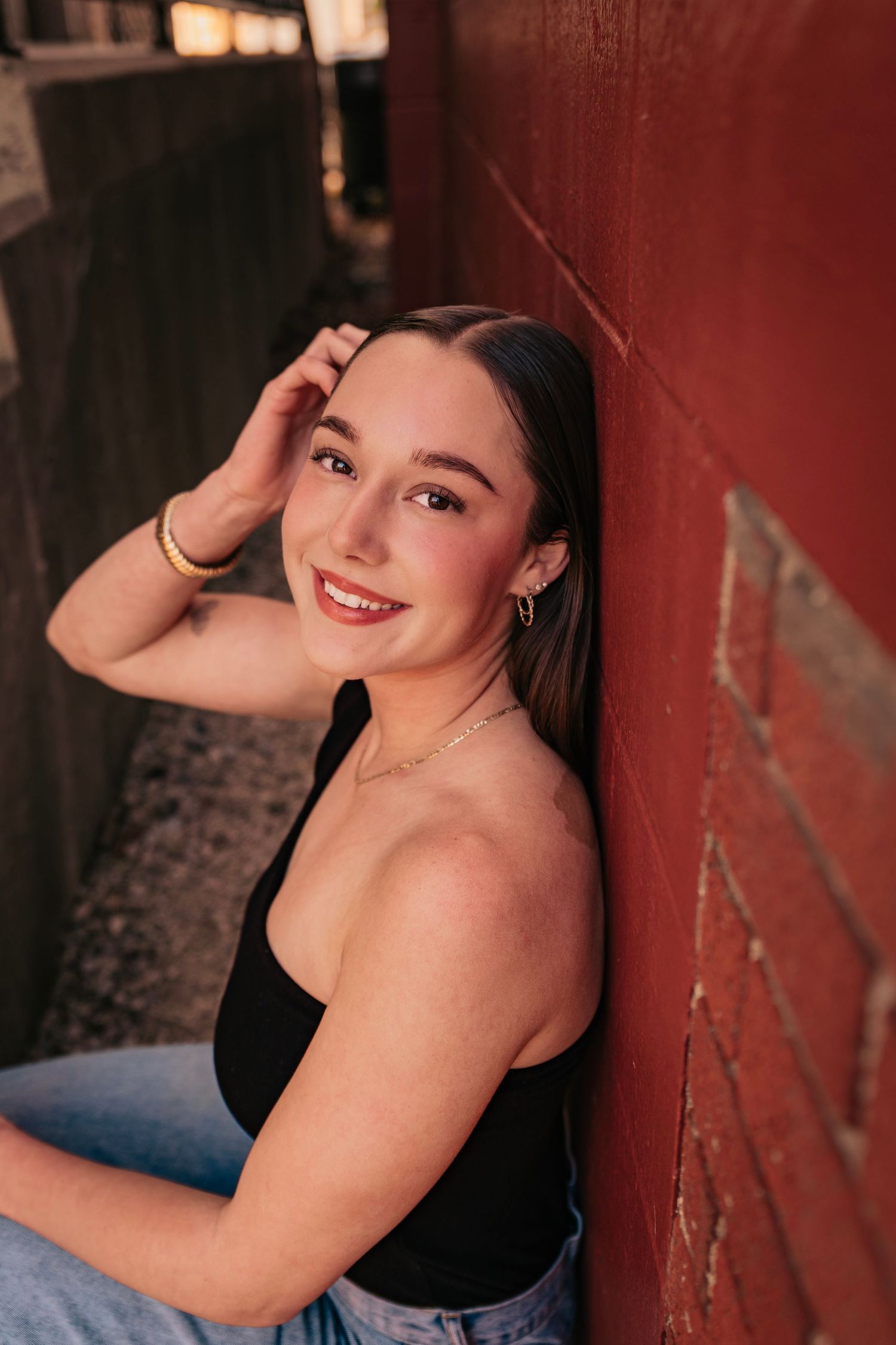 Portrait series against red brick wall showing casual poses in black tank top.