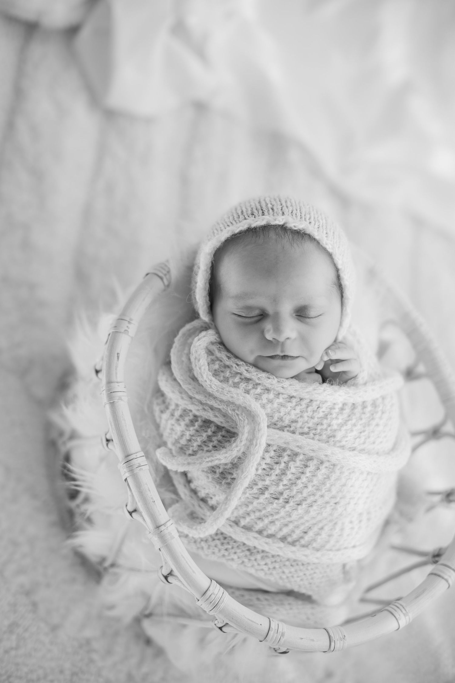 Newborn sleeping peacefully in white knit wrap on curved prop.