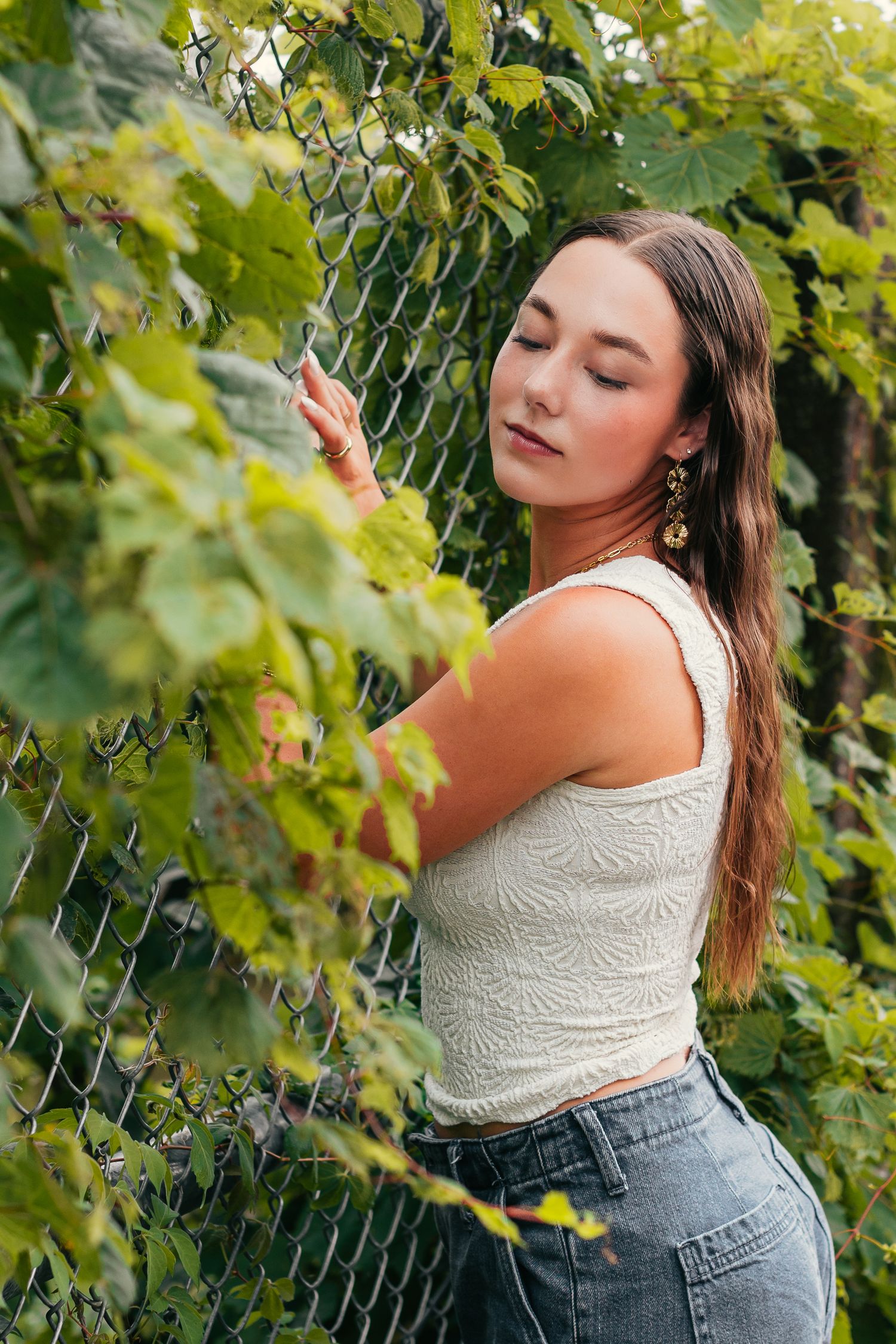 Person in white tank top touching grape vines on chain link fence.