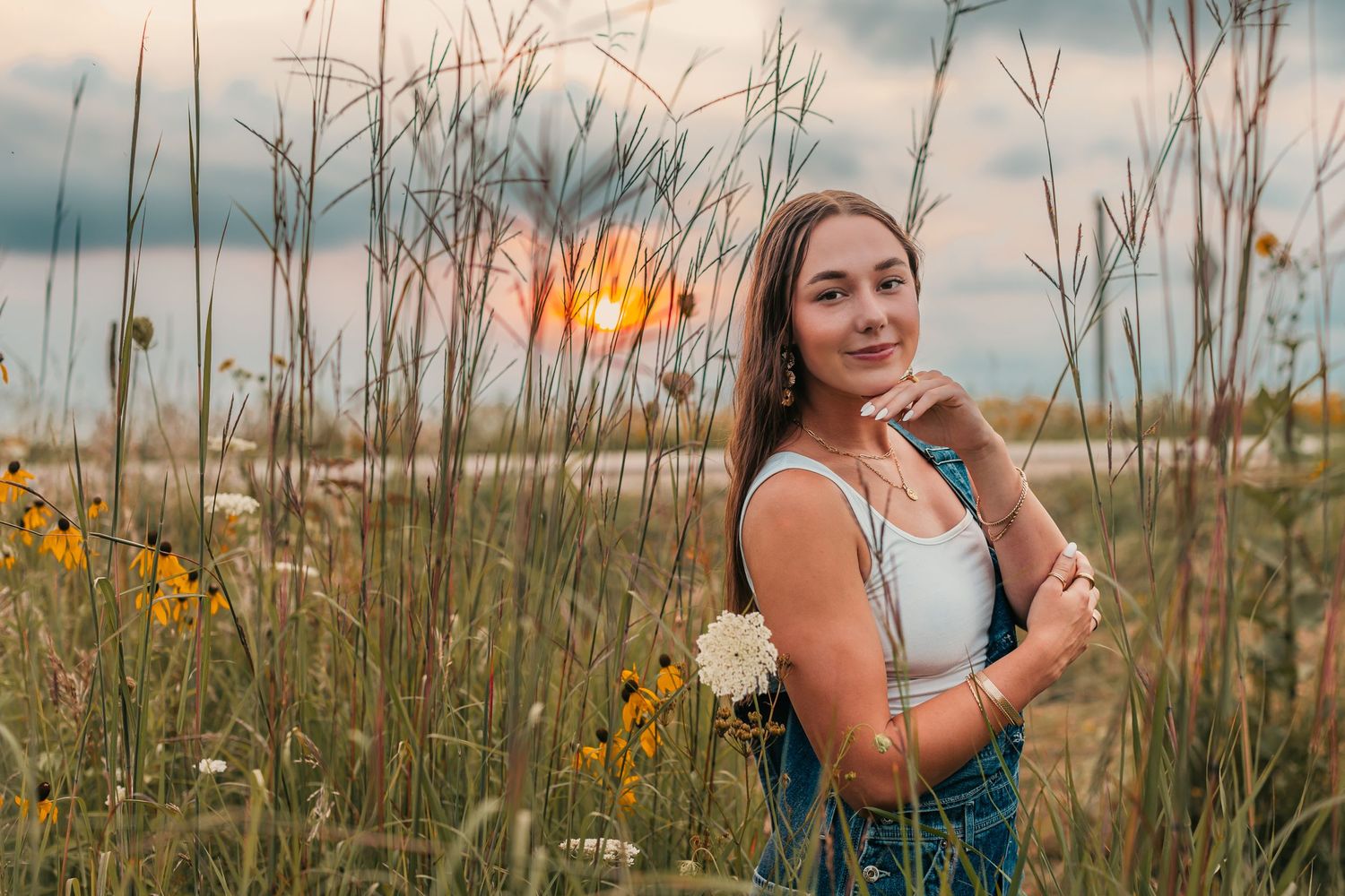 Portrait in wildflower field during golden hour with tall grass and cloudy sky.