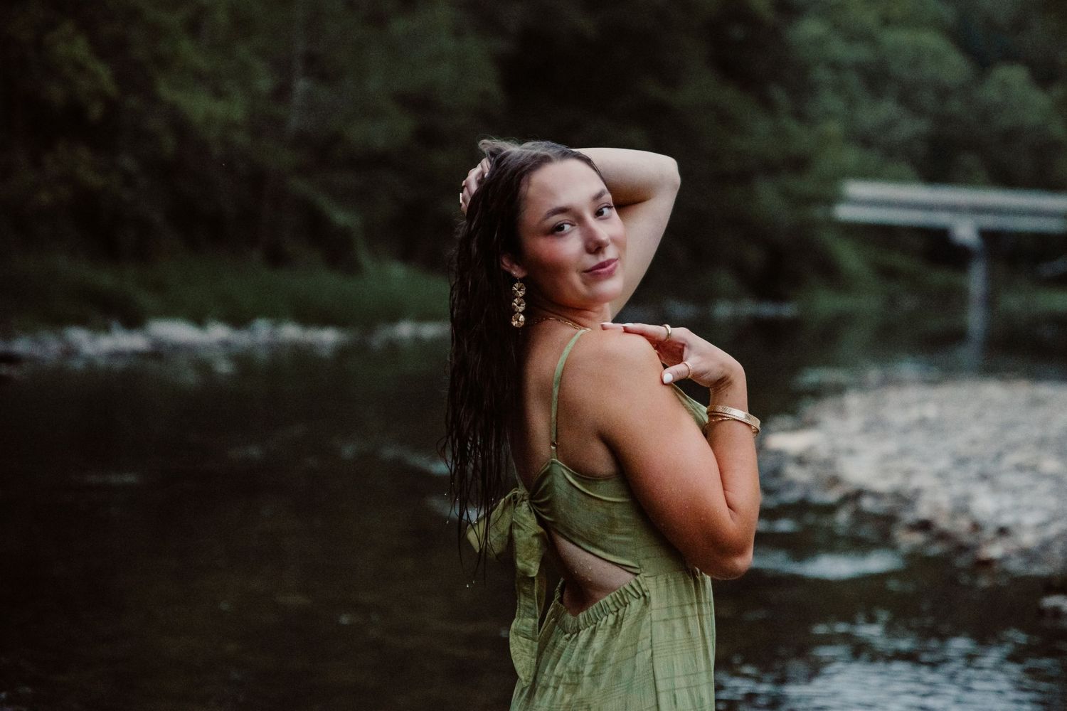 A romantic portrait of someone in a green dress posing by a river in moody lighting.