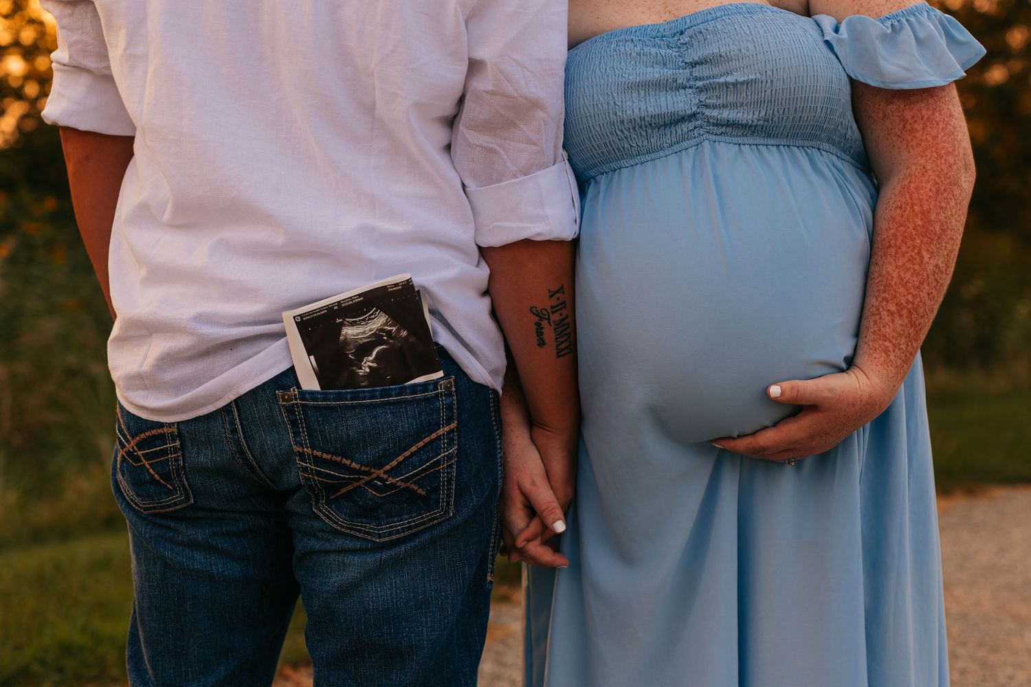 Maternity photo showing couple in white and blue outfits at sunset.