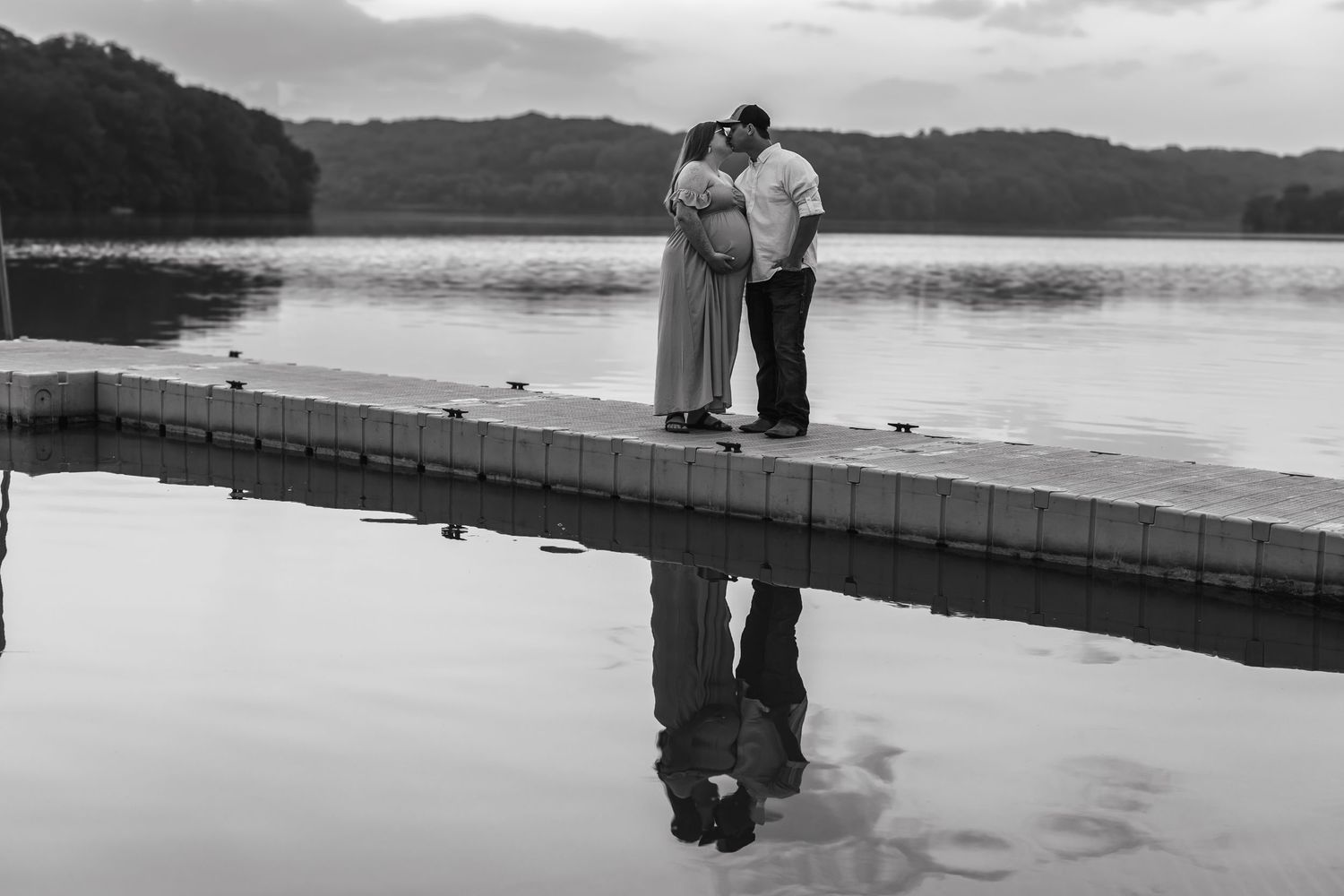 Silhouettes of people on wooden dock by lake at sunset.