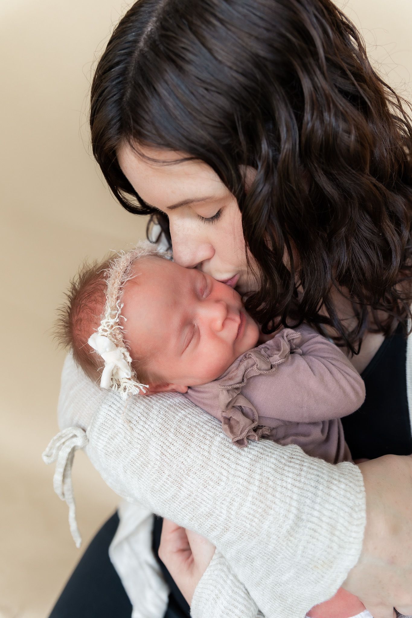 Tender moment between mother and sleeping newborn in soft natural light.