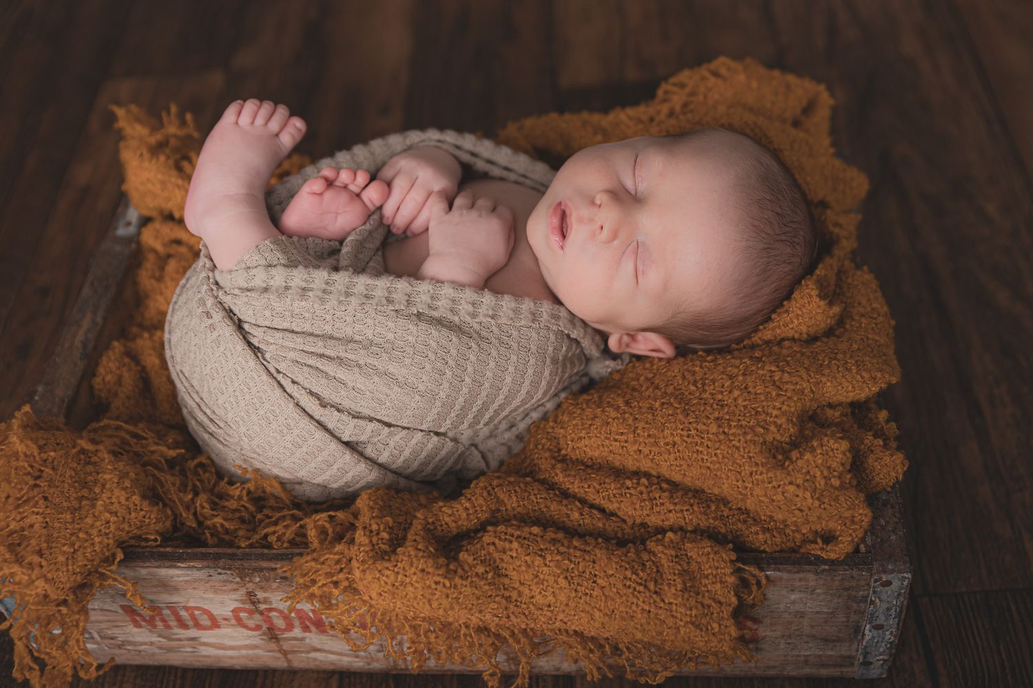 Sleeping newborn wrapped in cozy brown blanket during professional photography session.