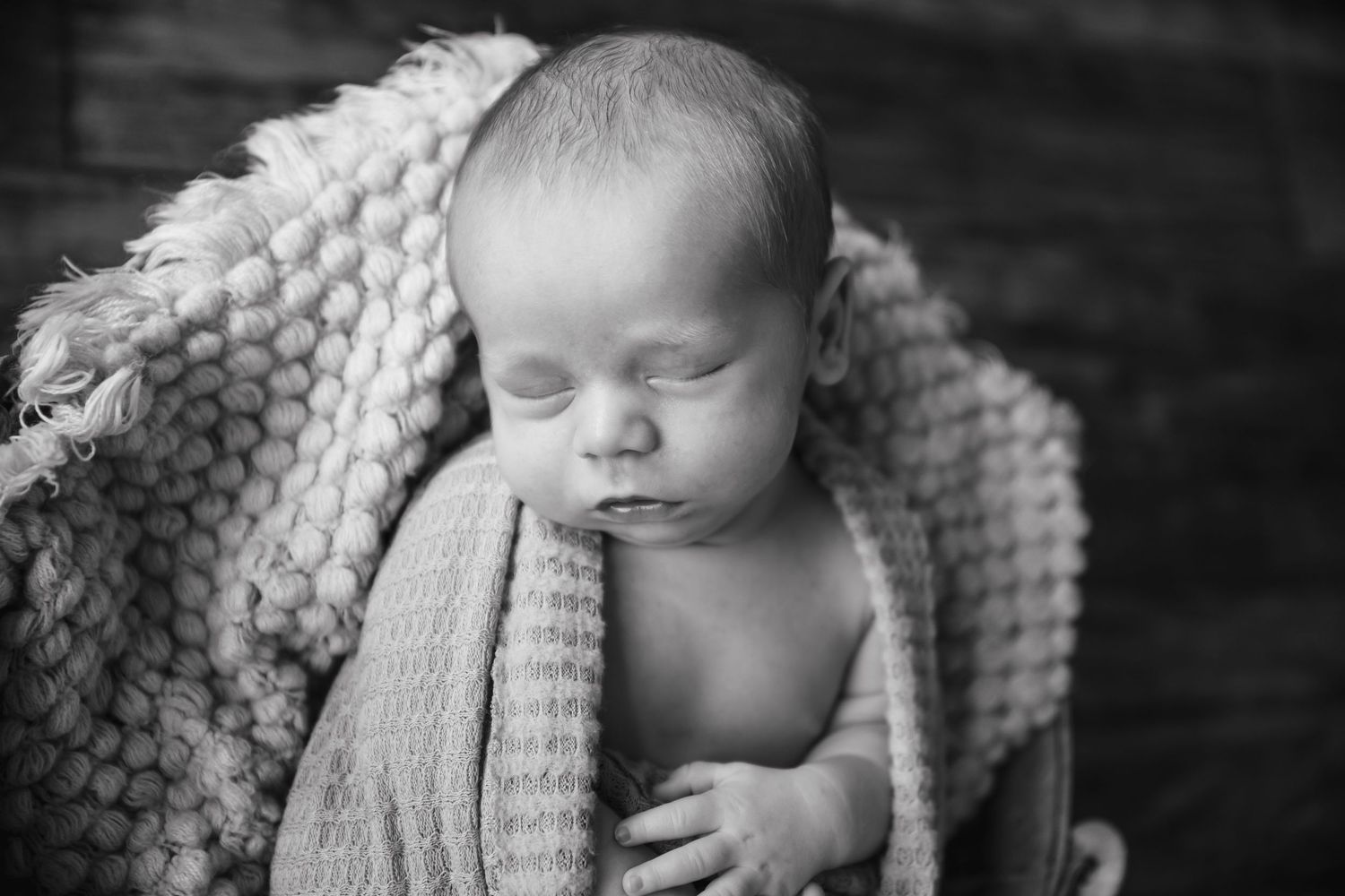 Peaceful sleeping newborn wrapped in chunky knit blanket.