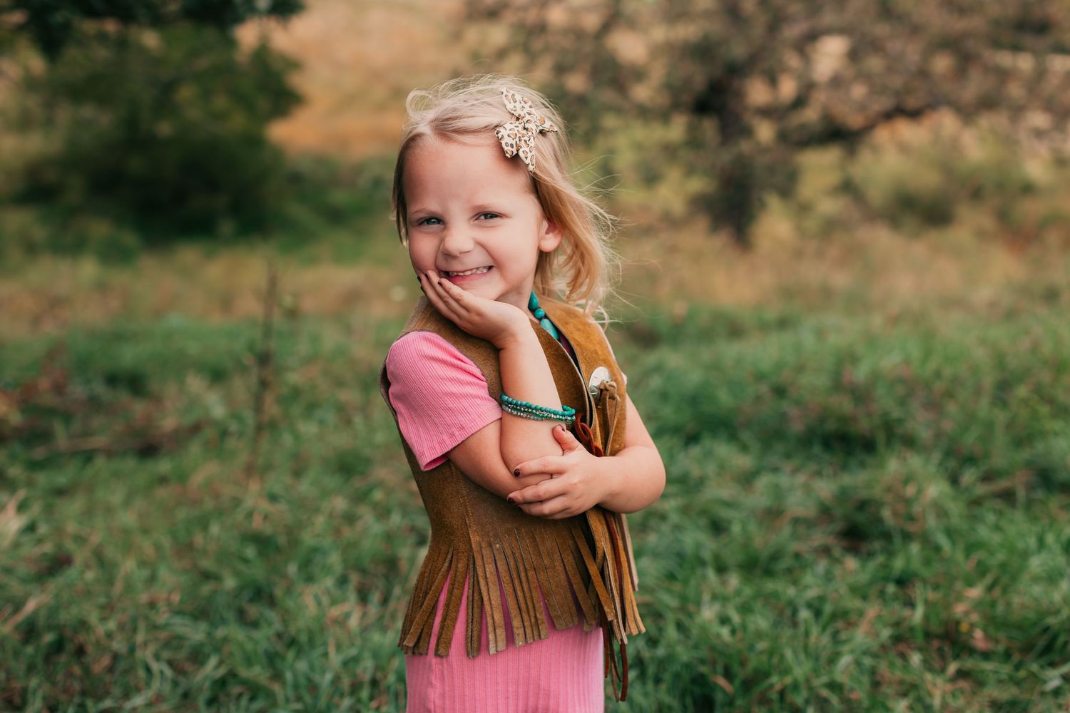 Child wearing pink shirt and fringe vest plays outdoors in golden sunlight.