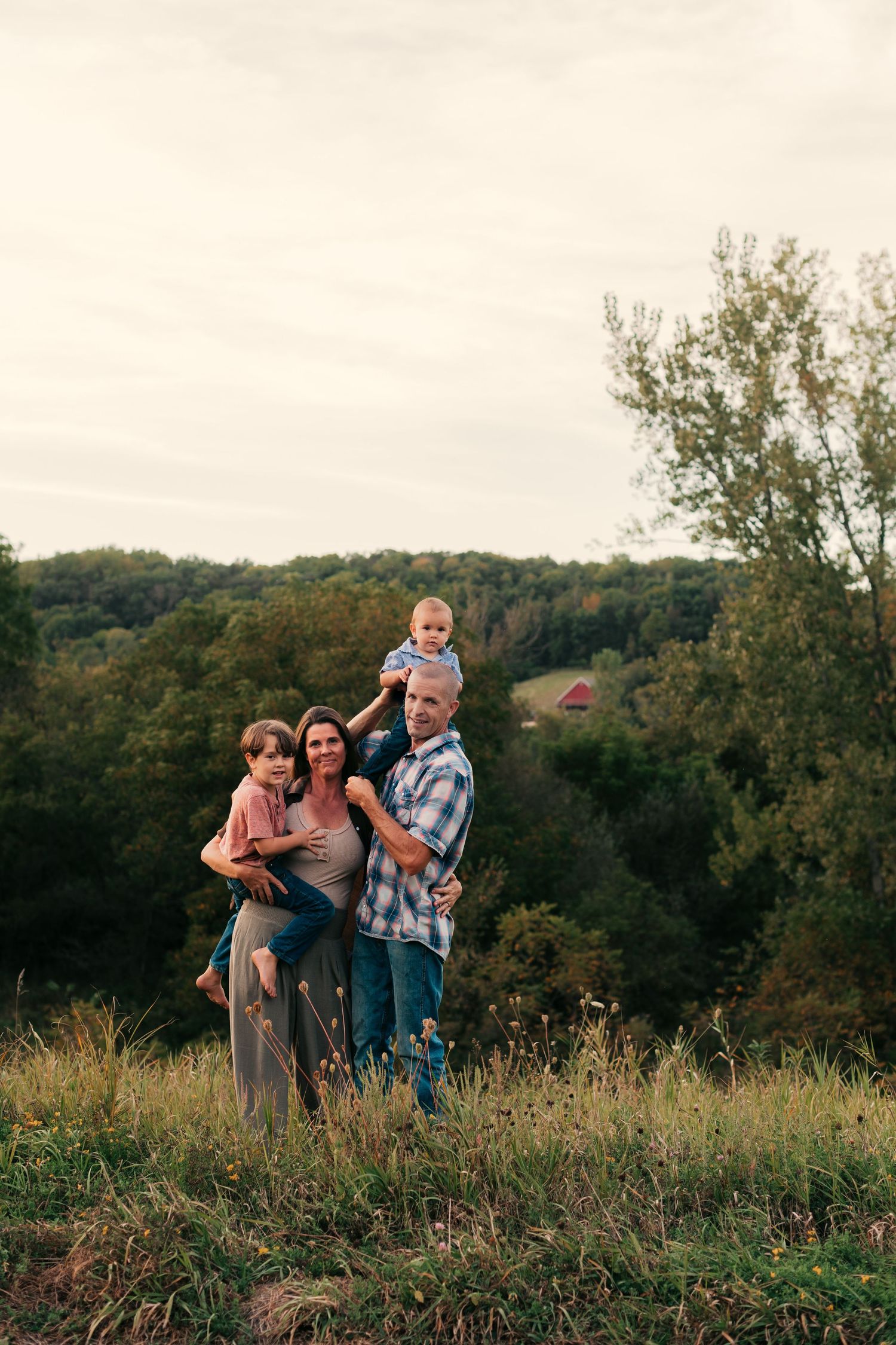Family stands together on hilltop overlooking autumn forest landscape.