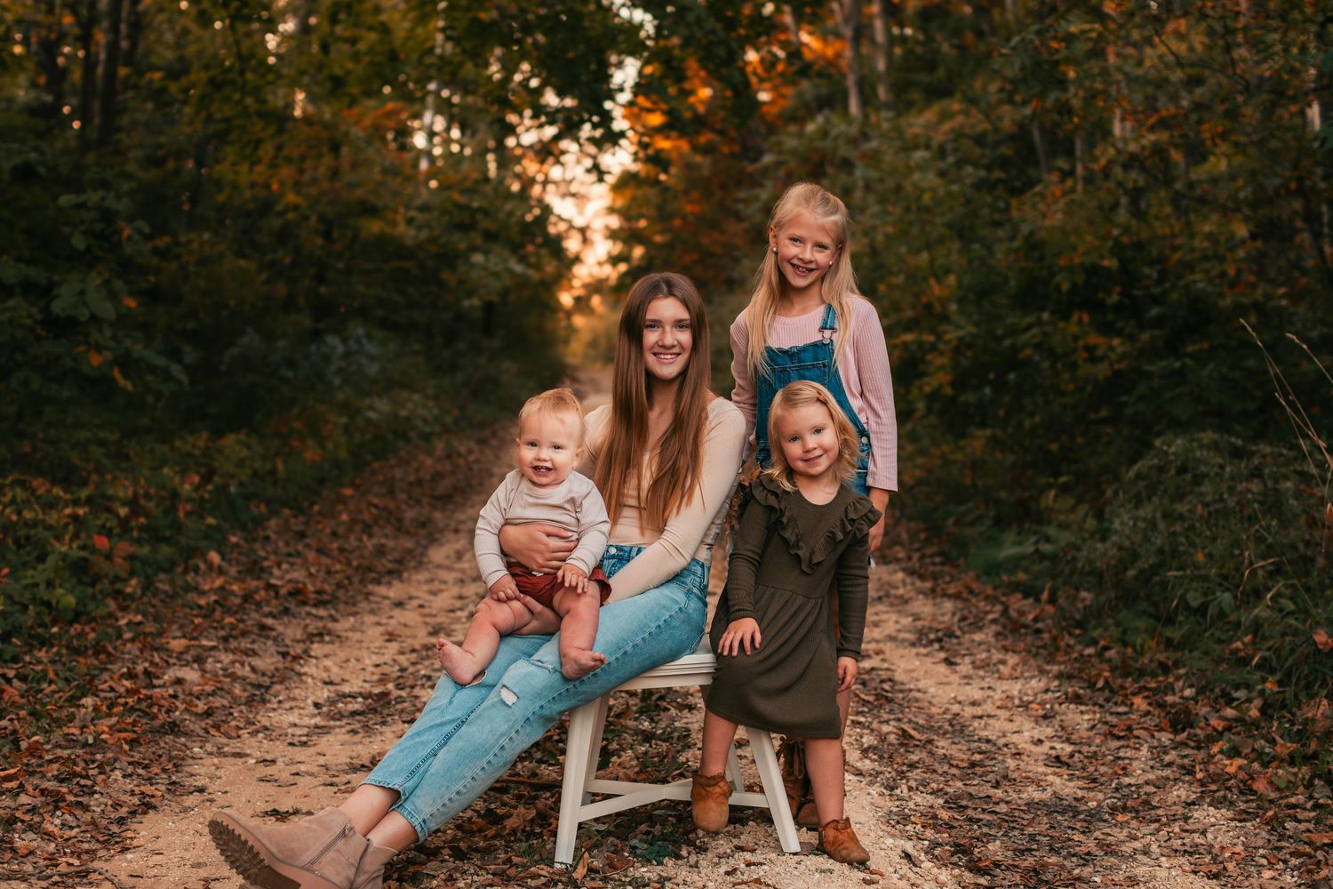 Family sitting on a rustic wooden bench in a sunlit wooded path during autumn.