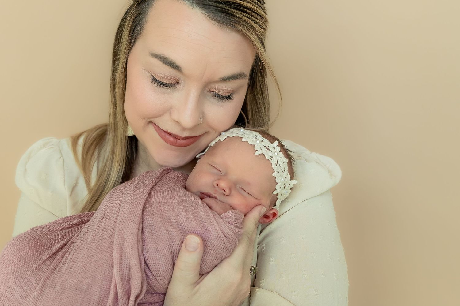 Peaceful sleeping newborn wrapped in soft pink swaddle against neutral background.