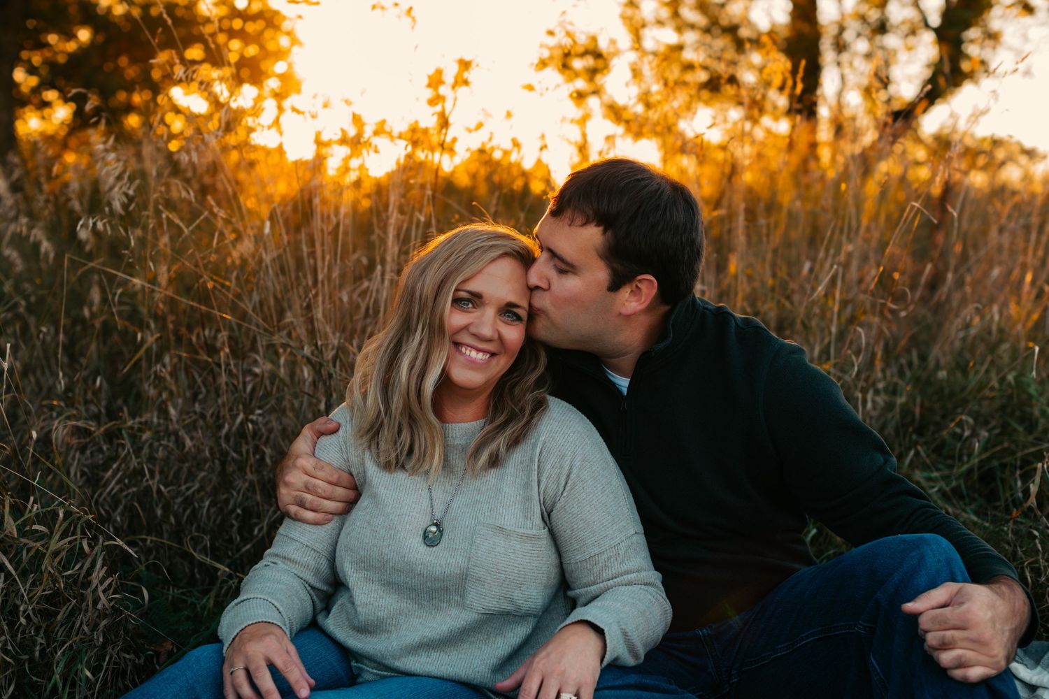 Couple sharing an intimate moment while sitting in tall grass during sunset.