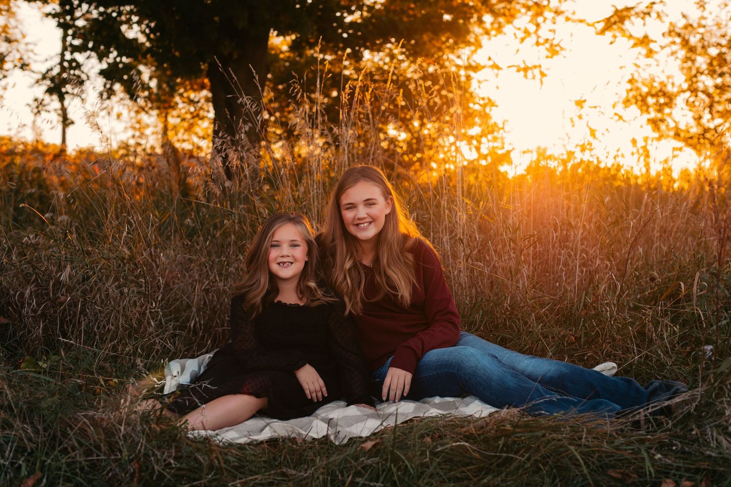 Two figures sitting on a blanket in a field at golden sunset with warm autumn colors.