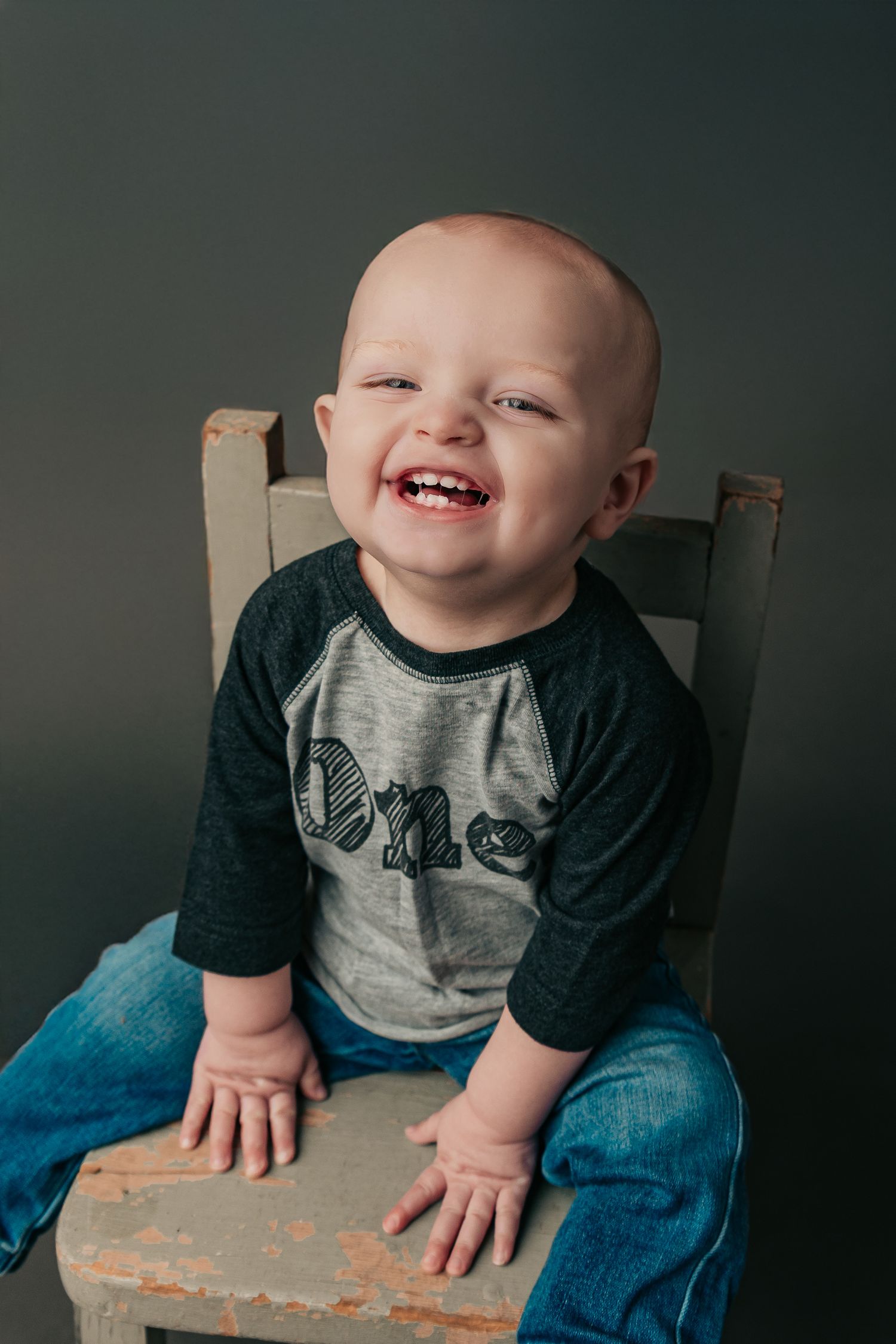 Young child sitting on wooden surface wearing raglan t-shirt and jeans.