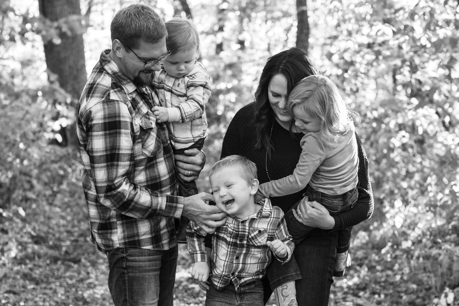 Family laughing together during casual black and white photo session in woods.