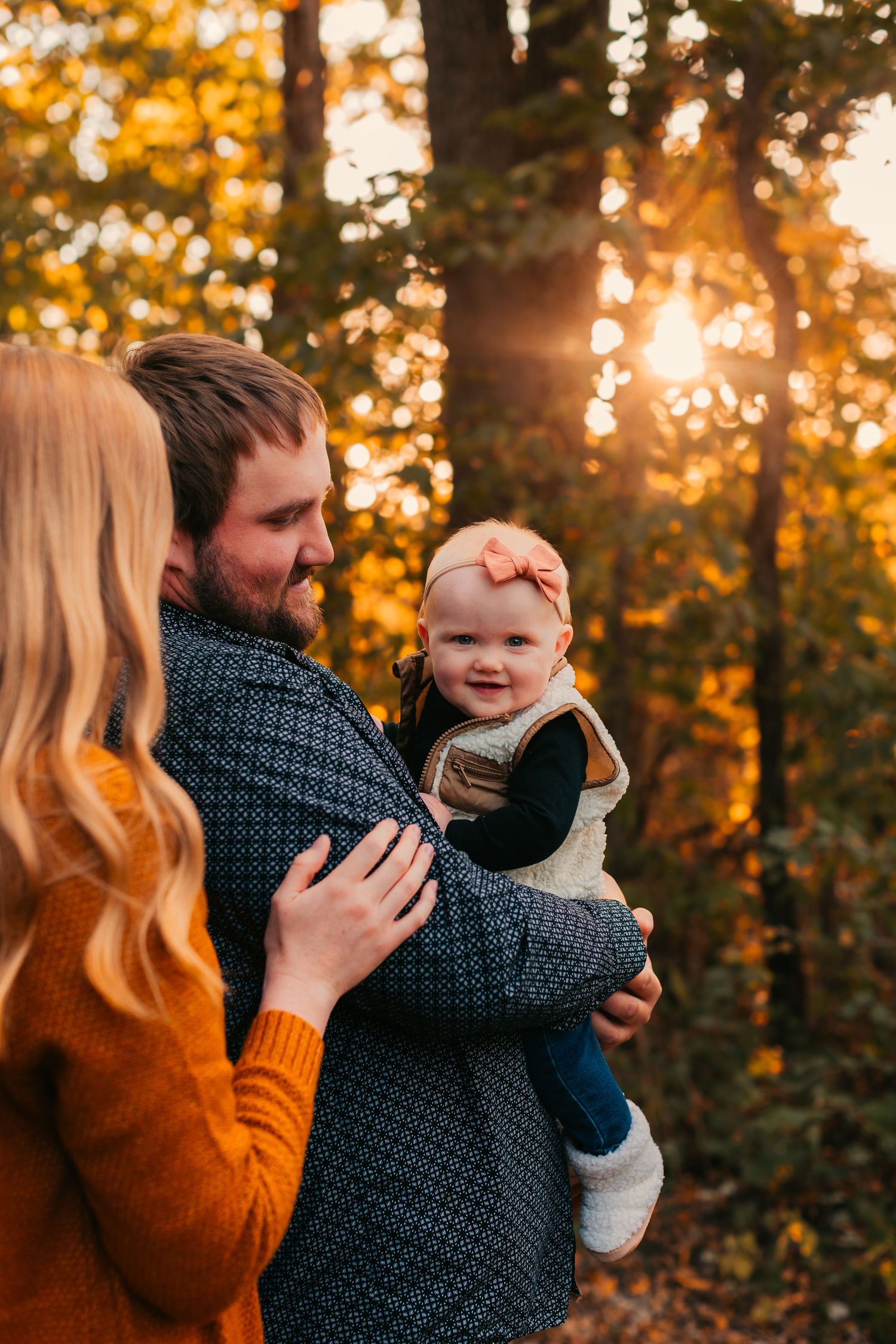 Family shares tender moment in autumn forest during golden hour.