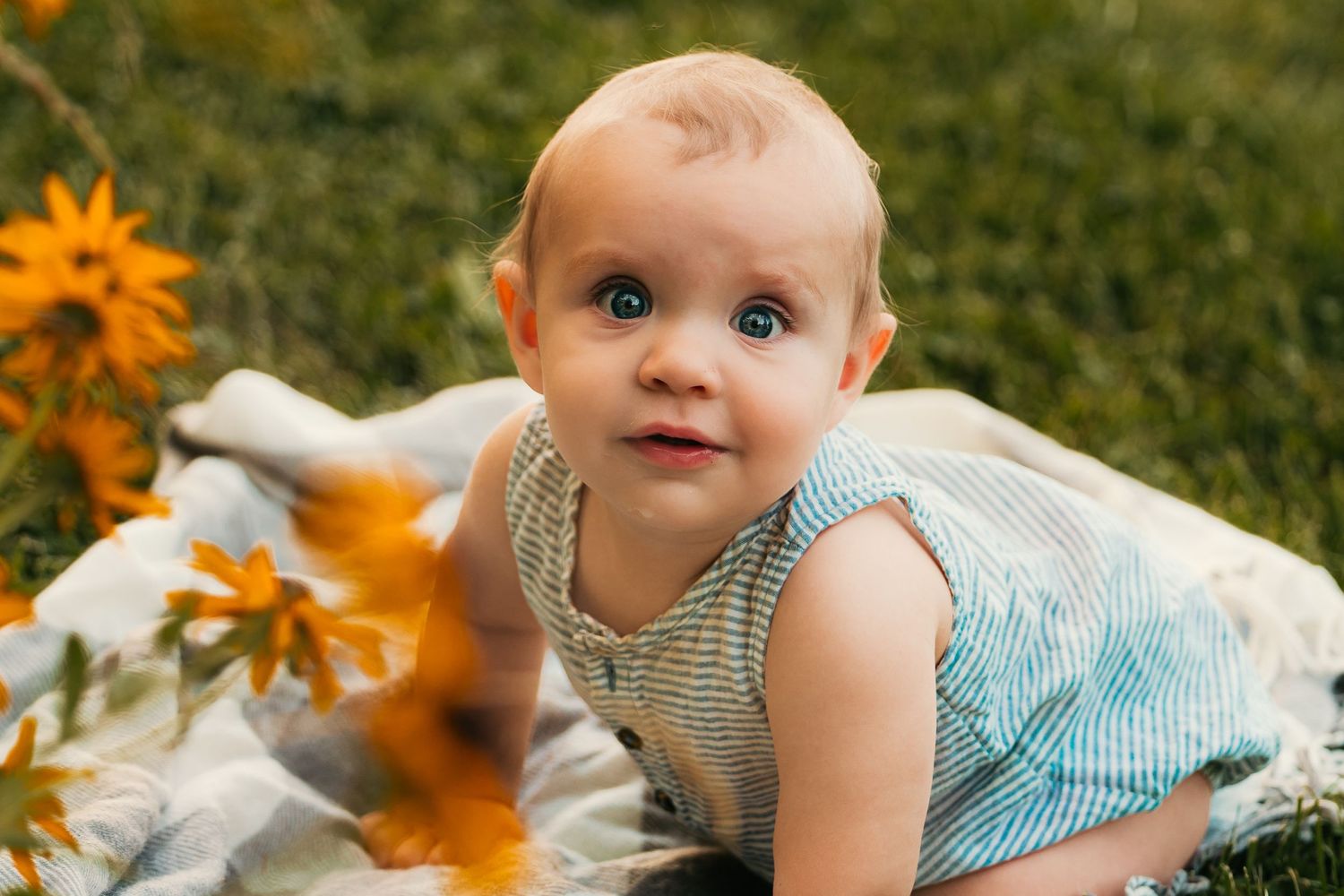 Baby lying on blanket outdoors with sunflowers in summer setting.