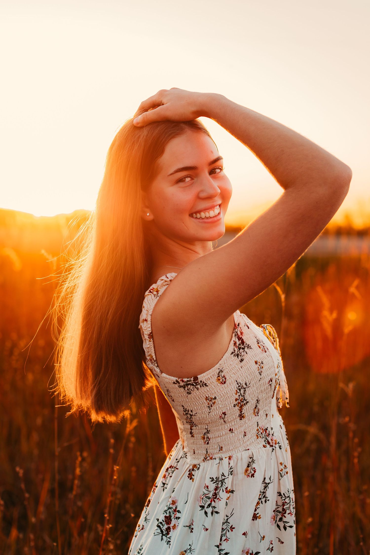 Young woman in floral dress poses in golden sunlit field at sunset.
