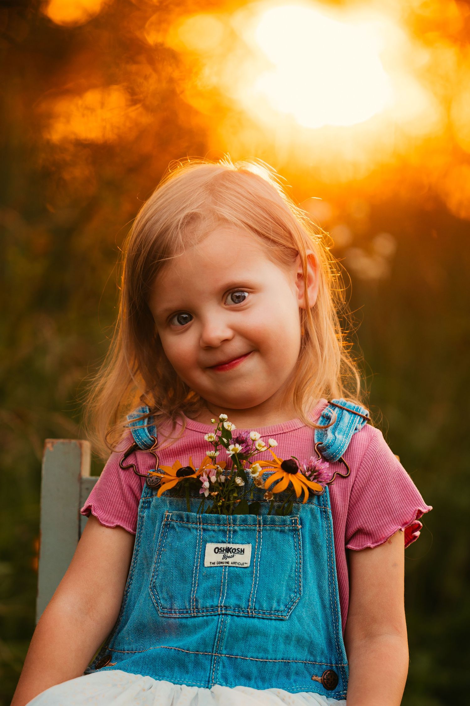Sunset portrait in warm golden light with sunflowers and denim overalls.
