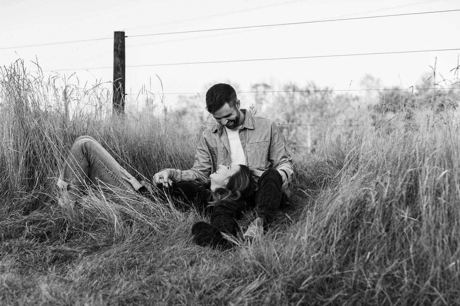 Couple relaxing together in tall grass field in black and white.