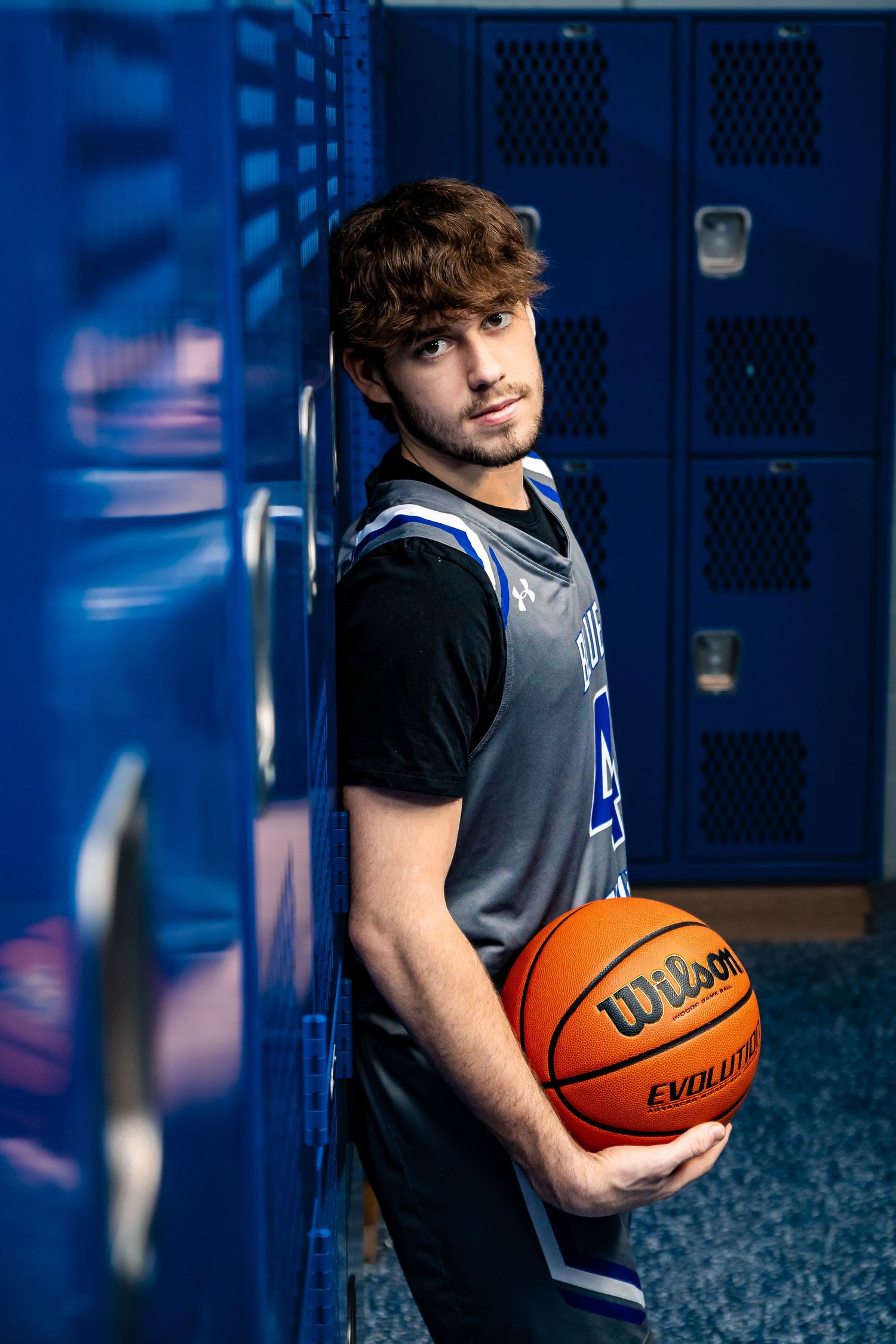 Basketball player poses with ball in front of blue lockers.