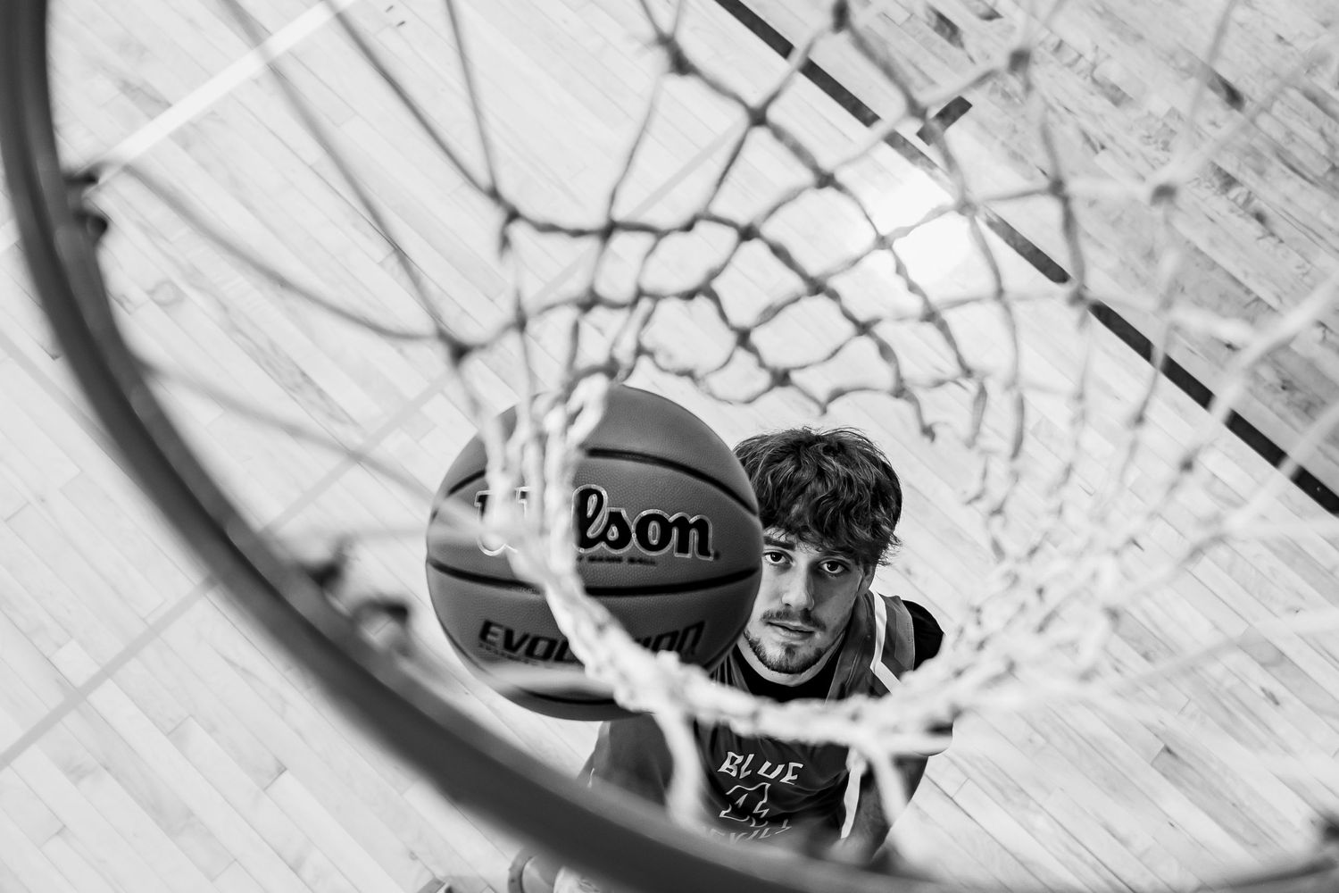 Looking up through a basketball hoop net in black and white.