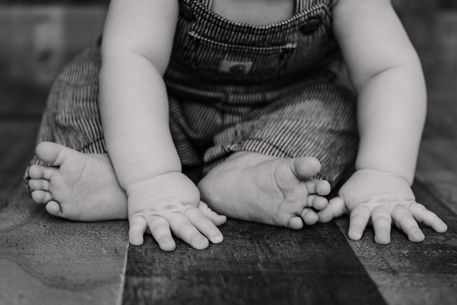 Close-up black and white photo of baby's hands and feet in striped overalls.