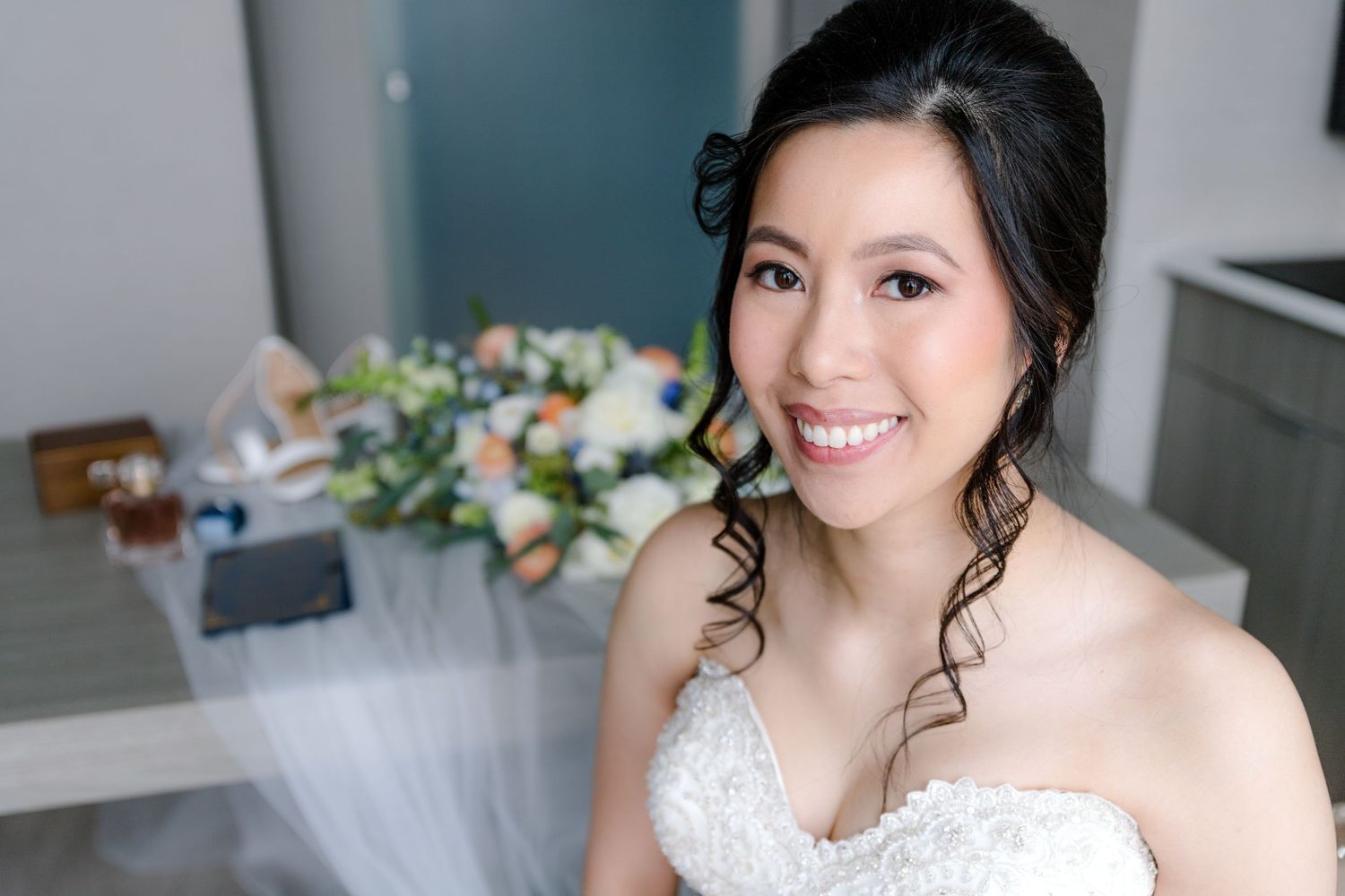 A bride in a white wedding dress poses elegantly in a light-filled room.