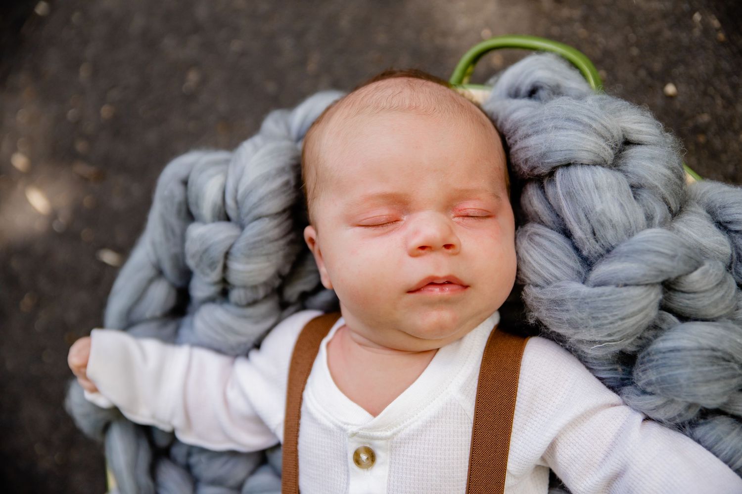 Sleeping newborn baby resting on soft gray knitted blanket wearing suspenders.