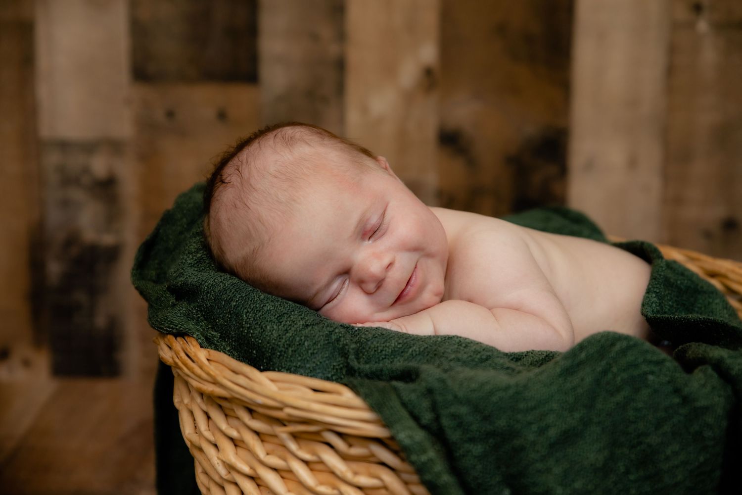Peaceful newborn baby sleeping in rustic basket with dark green blanket.