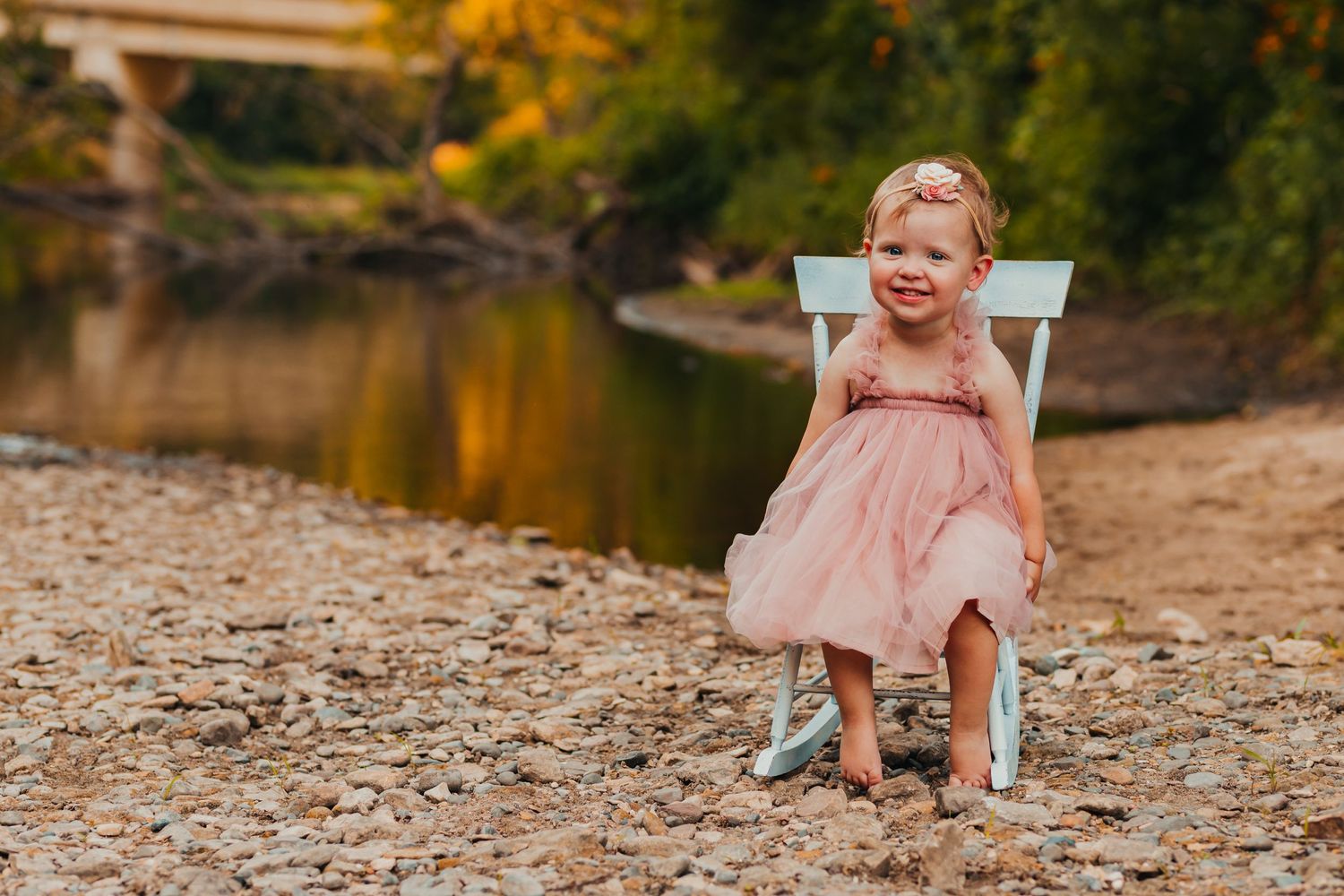 Family photoshoot by riverbank with autumn foliage in the background.