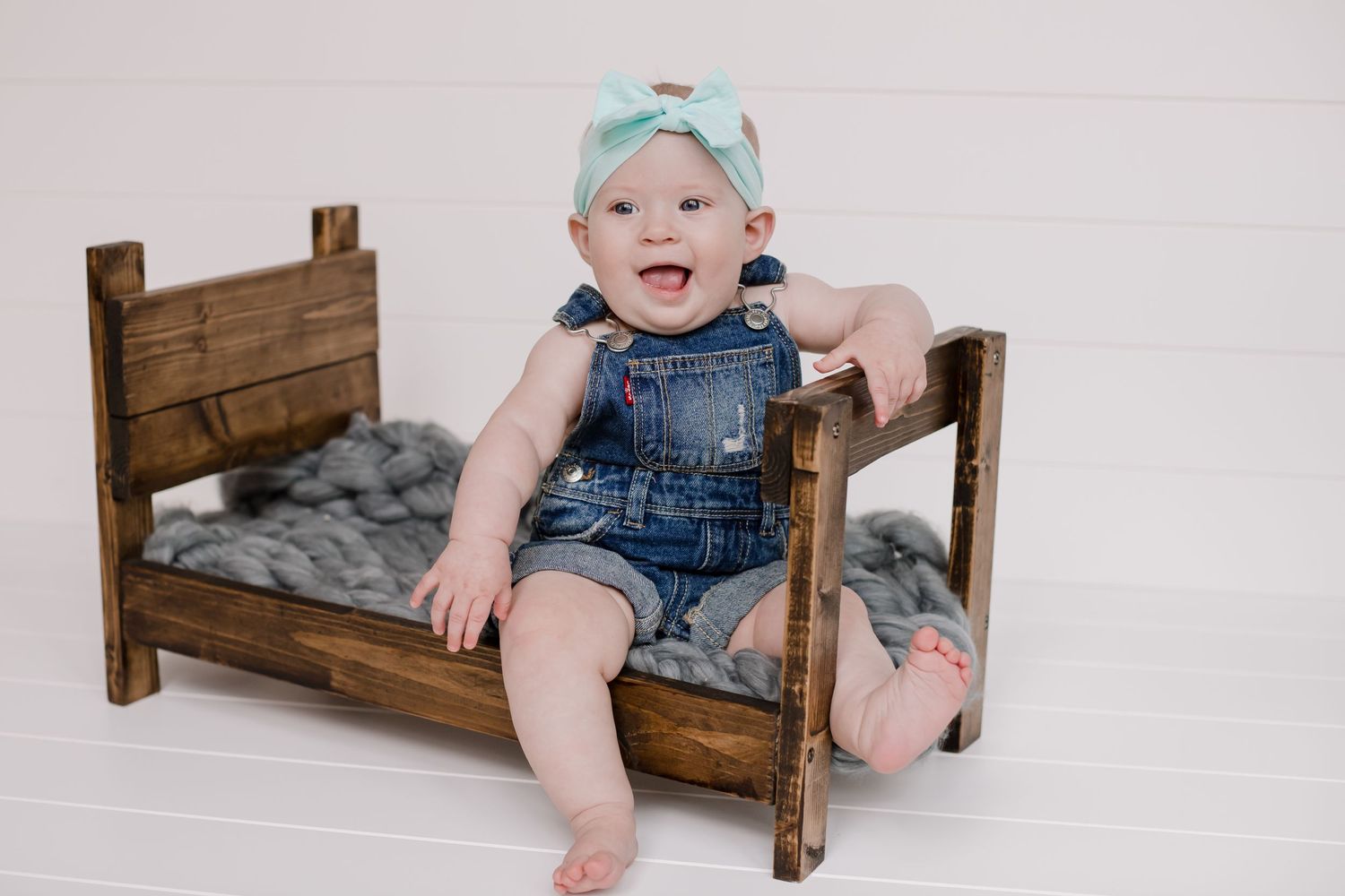 Small wooden bench prop with gray cushions for baby photography.