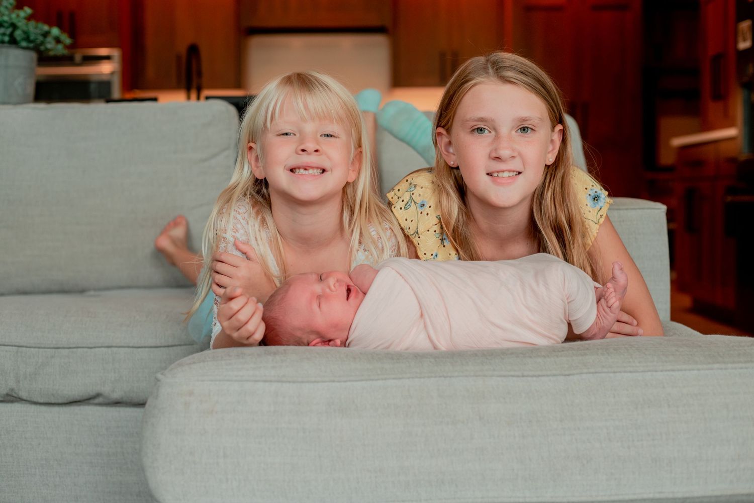 Three children lounging together on a grey couch.