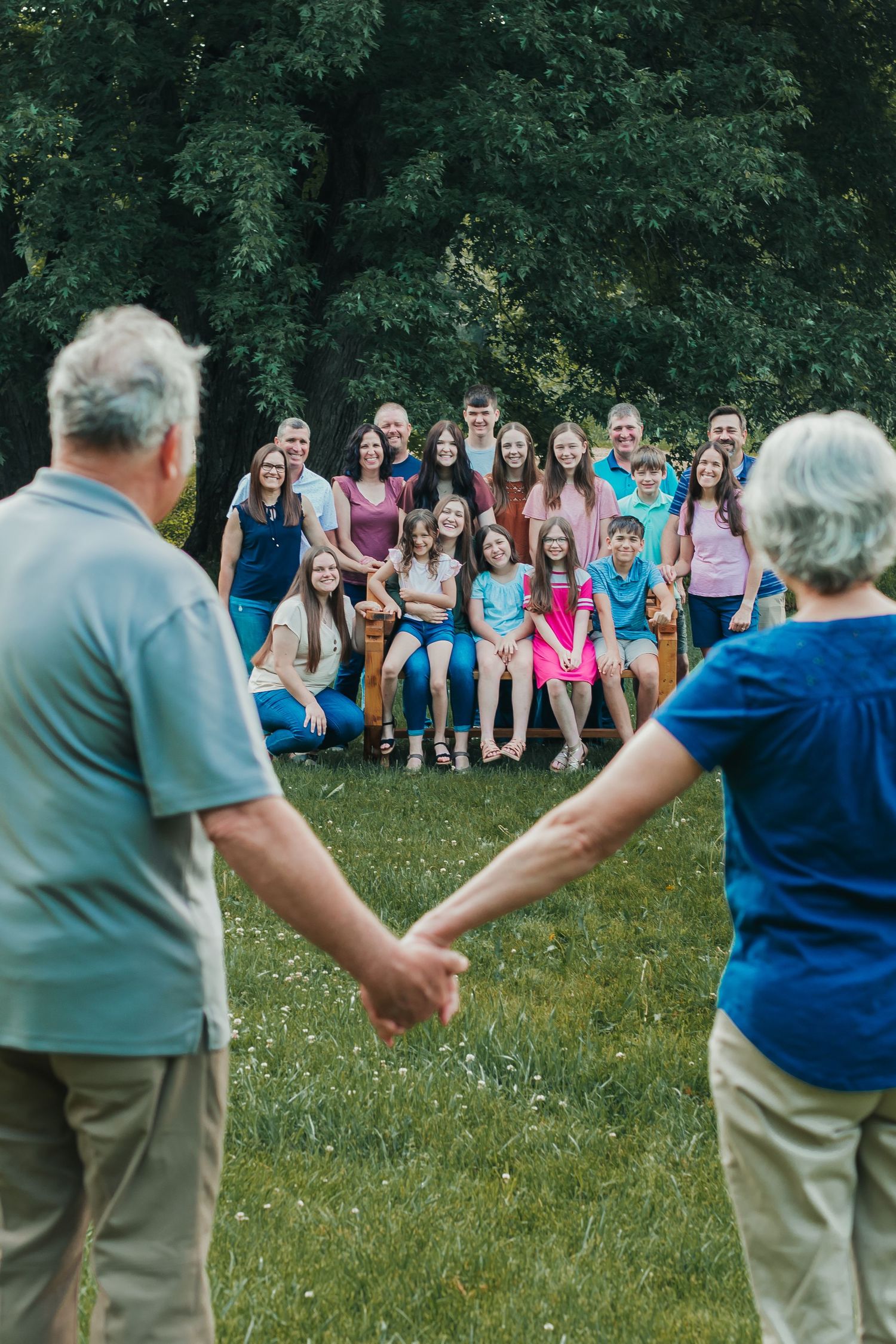 Multi-generational family photo with elderly couple holding hands in foreground and group behind them.