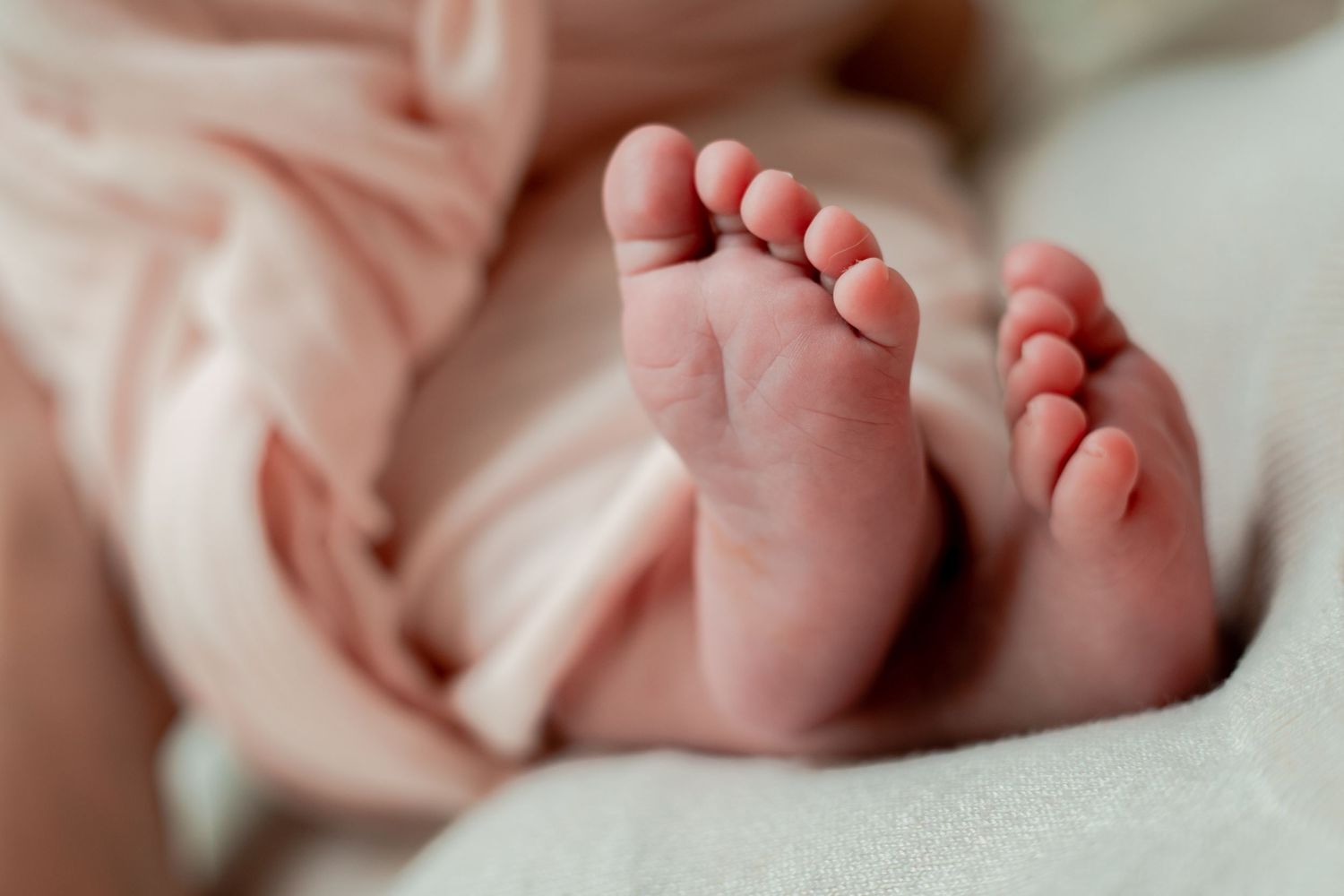 Close-up details of tiny newborn baby feet wrapped in soft pink blanket.