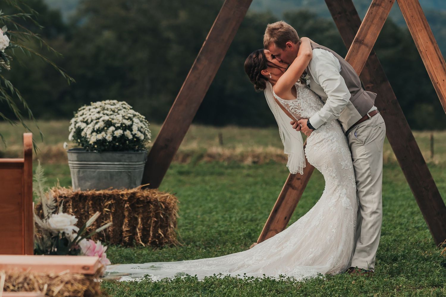 Romantic wedding couple posing under wooden arch in outdoor garden setting.