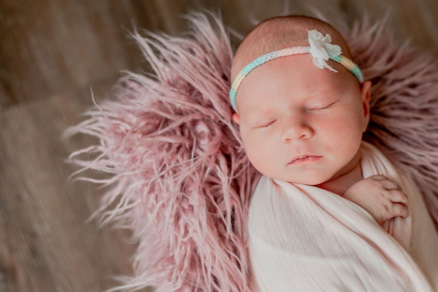 Sleeping newborn wrapped in white fabric on pink fluffy material.