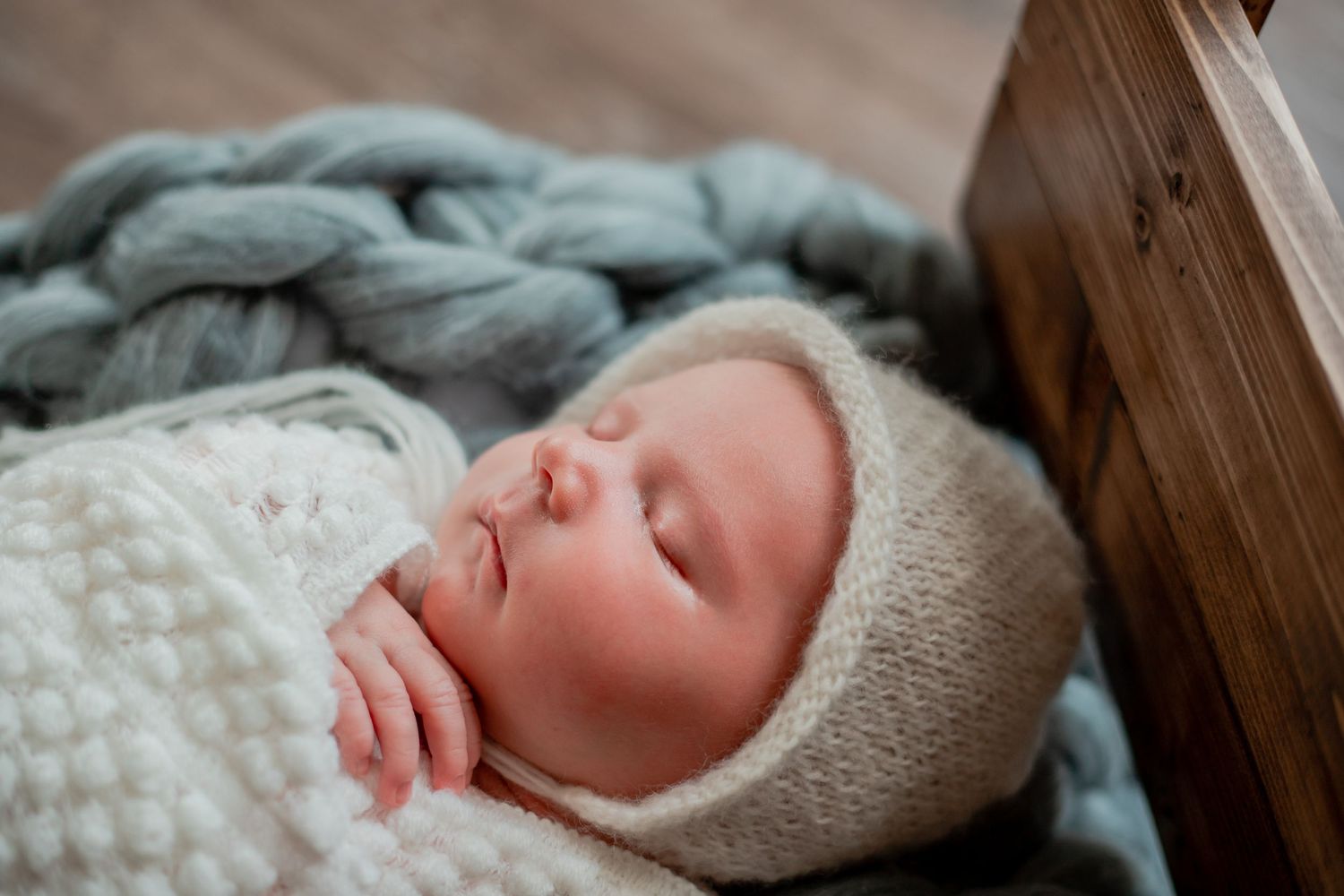Sleeping newborn wrapped in cozy white knit blanket during professional photo session.