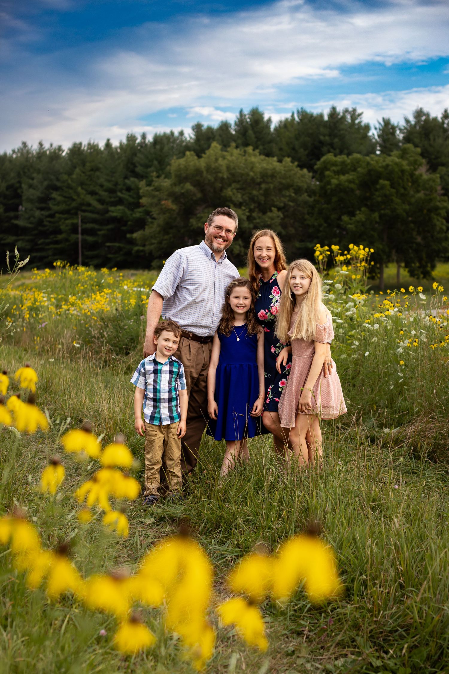 Family portrait series in a summer wildflower field with yellow blooms and blue sky.