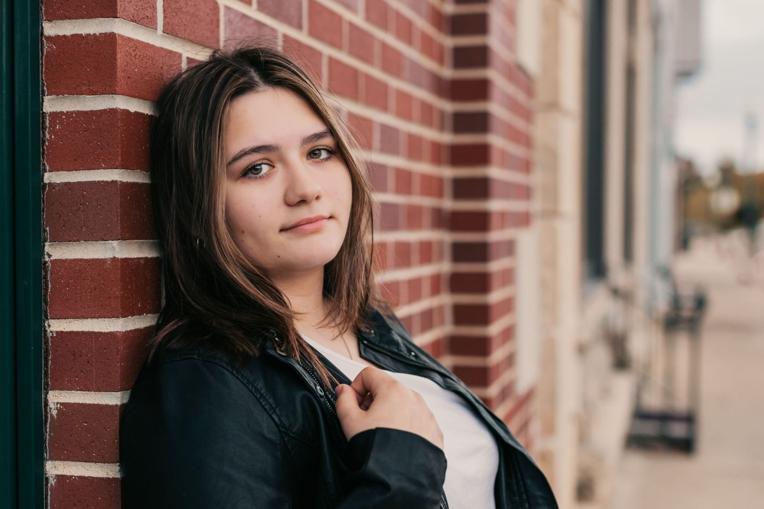 A portrait against a red brick wall wearing a black leather jacket.