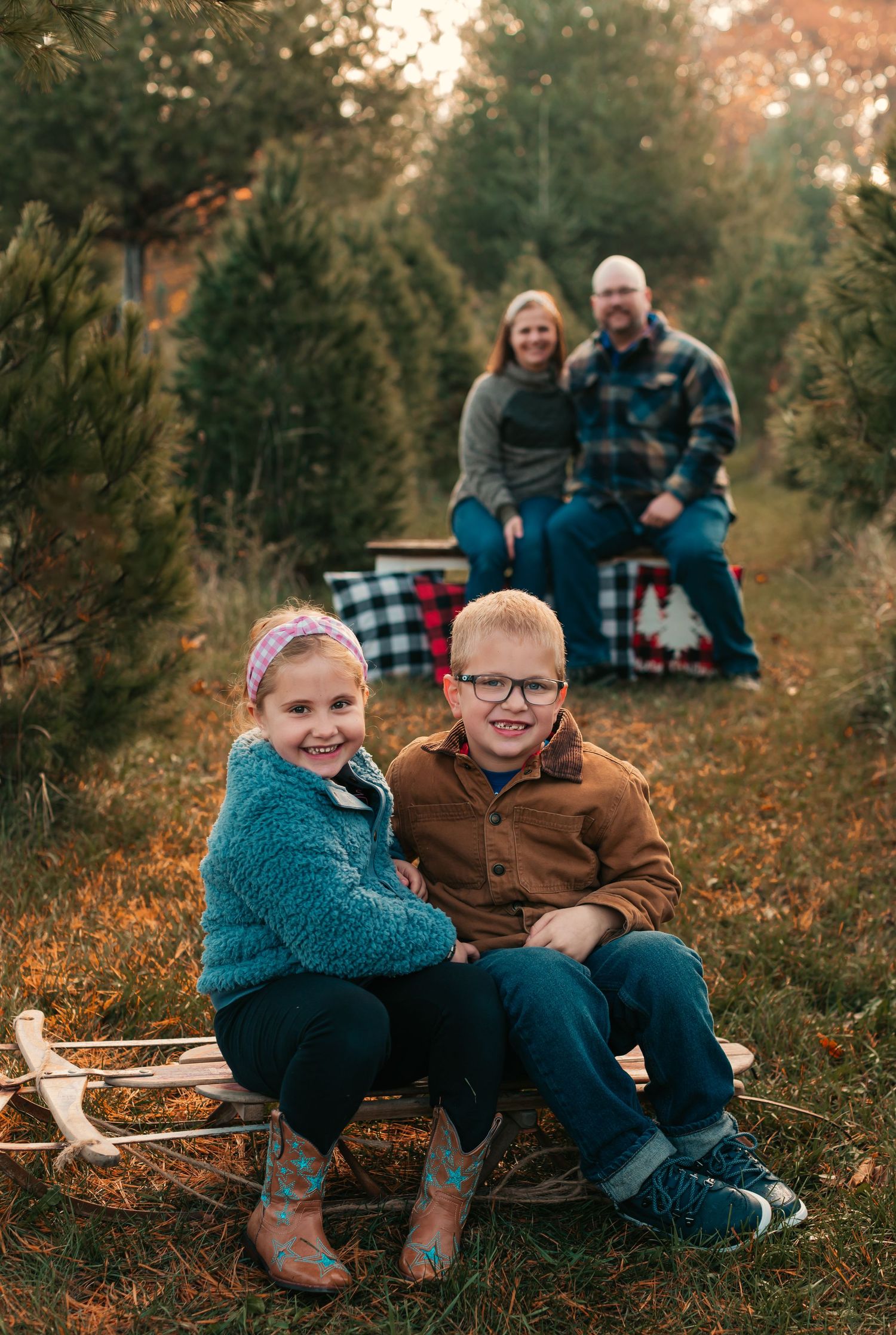 Family sitting together on grass at Christmas tree farm during sunset.