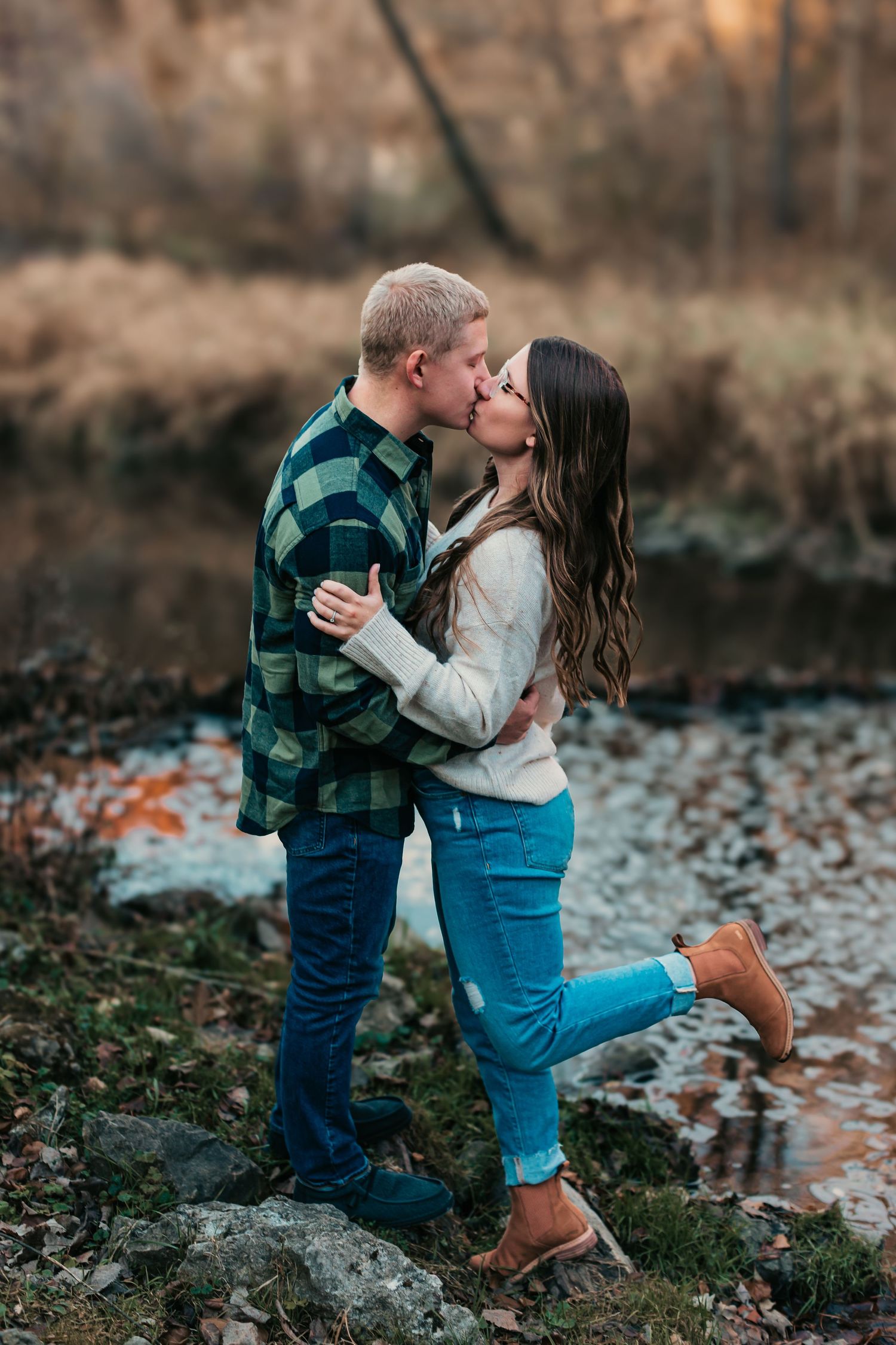Romantic couple sharing a kiss by a rocky creek in autumn.