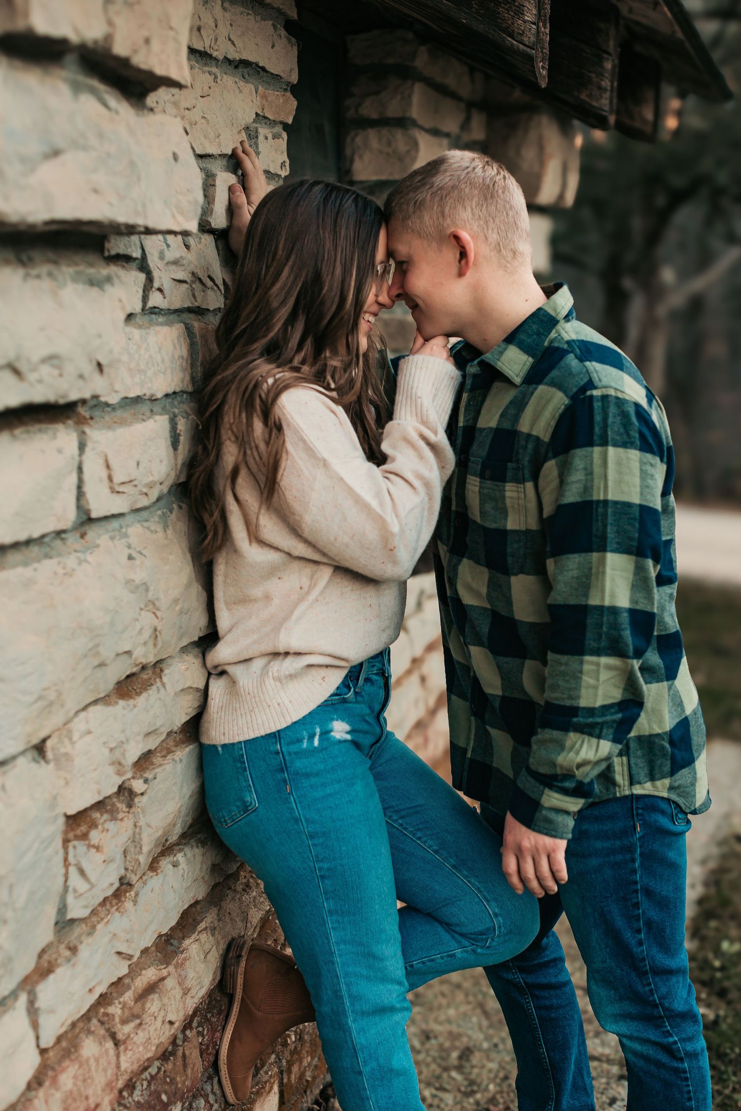 Intimate couple portrait against rustic stone wall wearing coordinating plaid and sweaters.