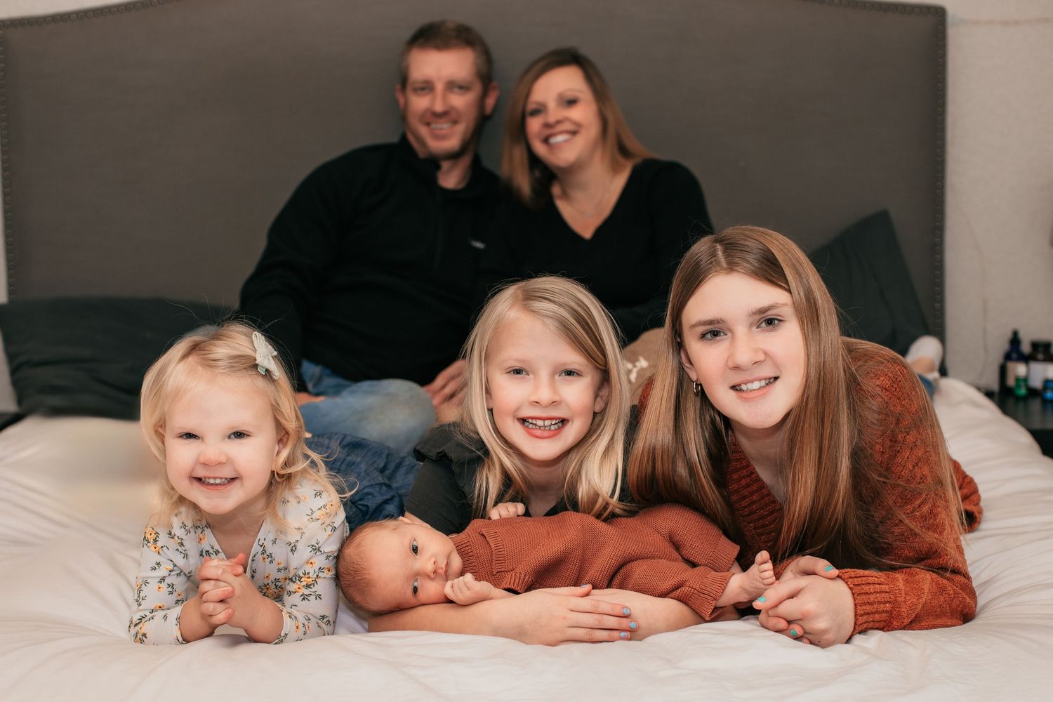 Family group portrait on bed with newborn baby.