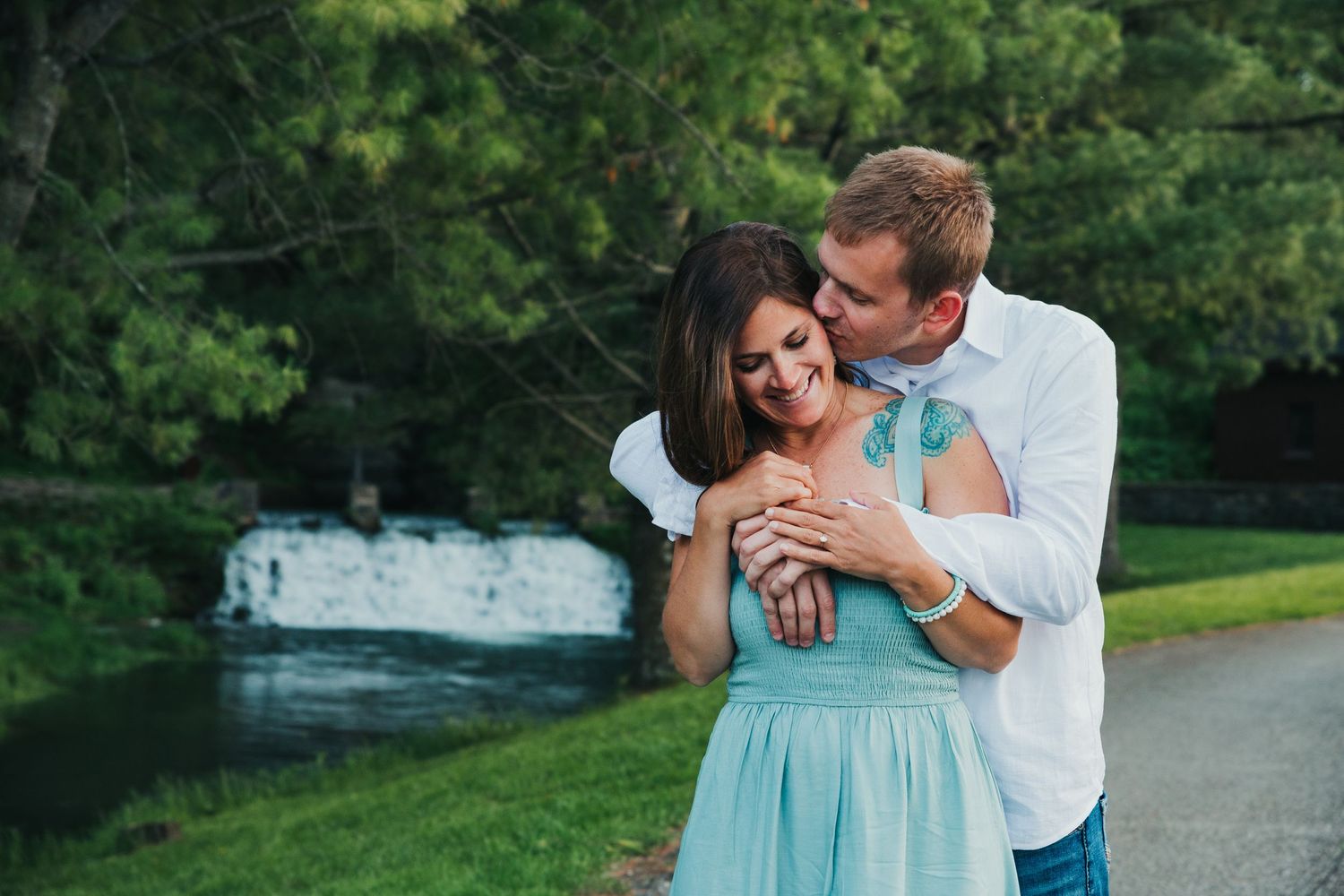 A romantic couple embracing in a park setting wearing blue and white outfits.